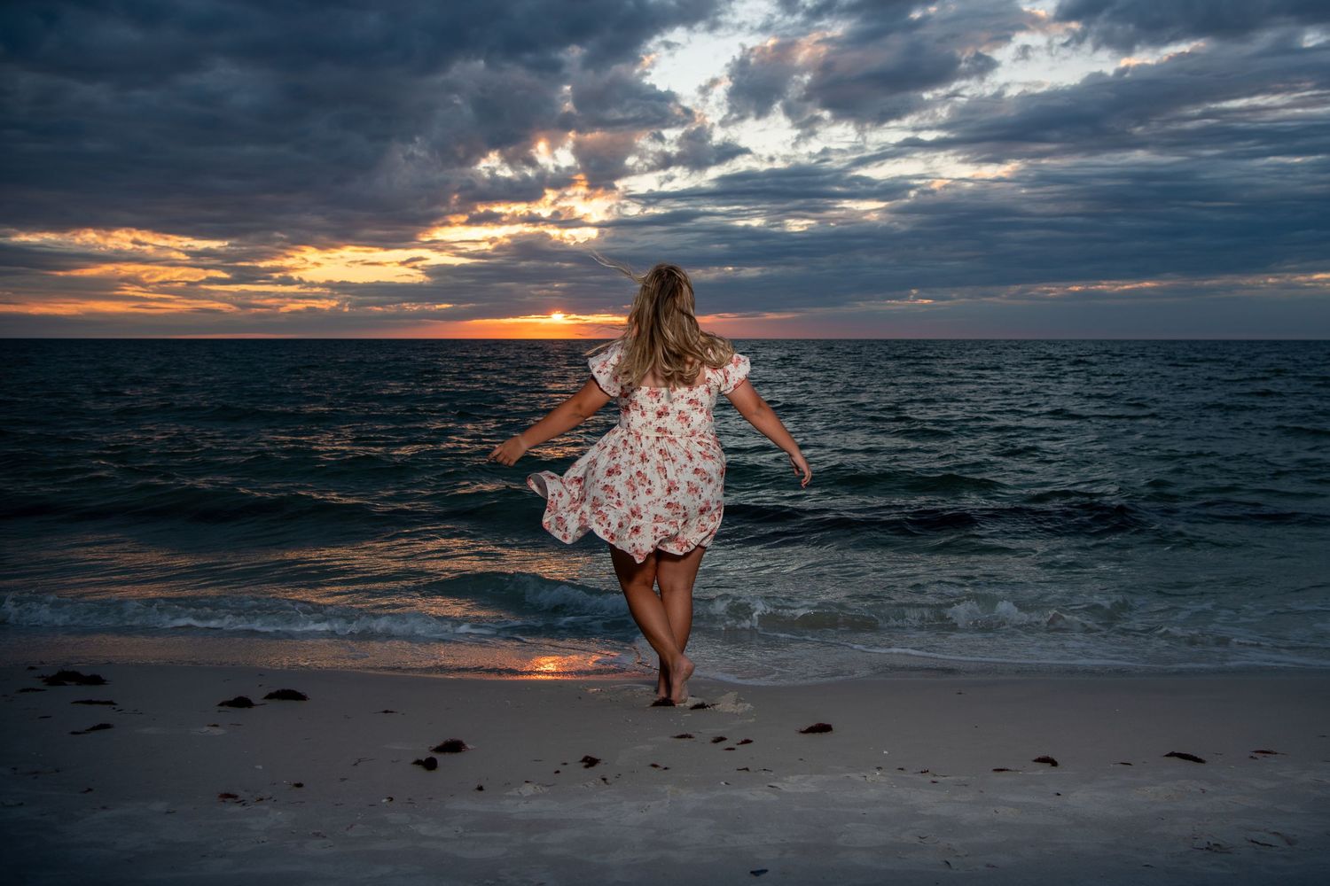 Dramatic sunset beach photoshoot with person in floral dress against cloudy sky. Self portraits. Senior photos.