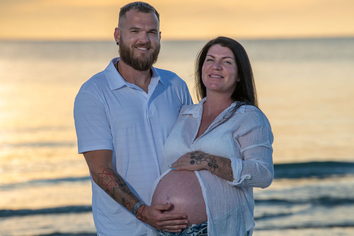 Expecting couple shares intimate moment on beach during golden hour sunset. Maternity photoshoot.