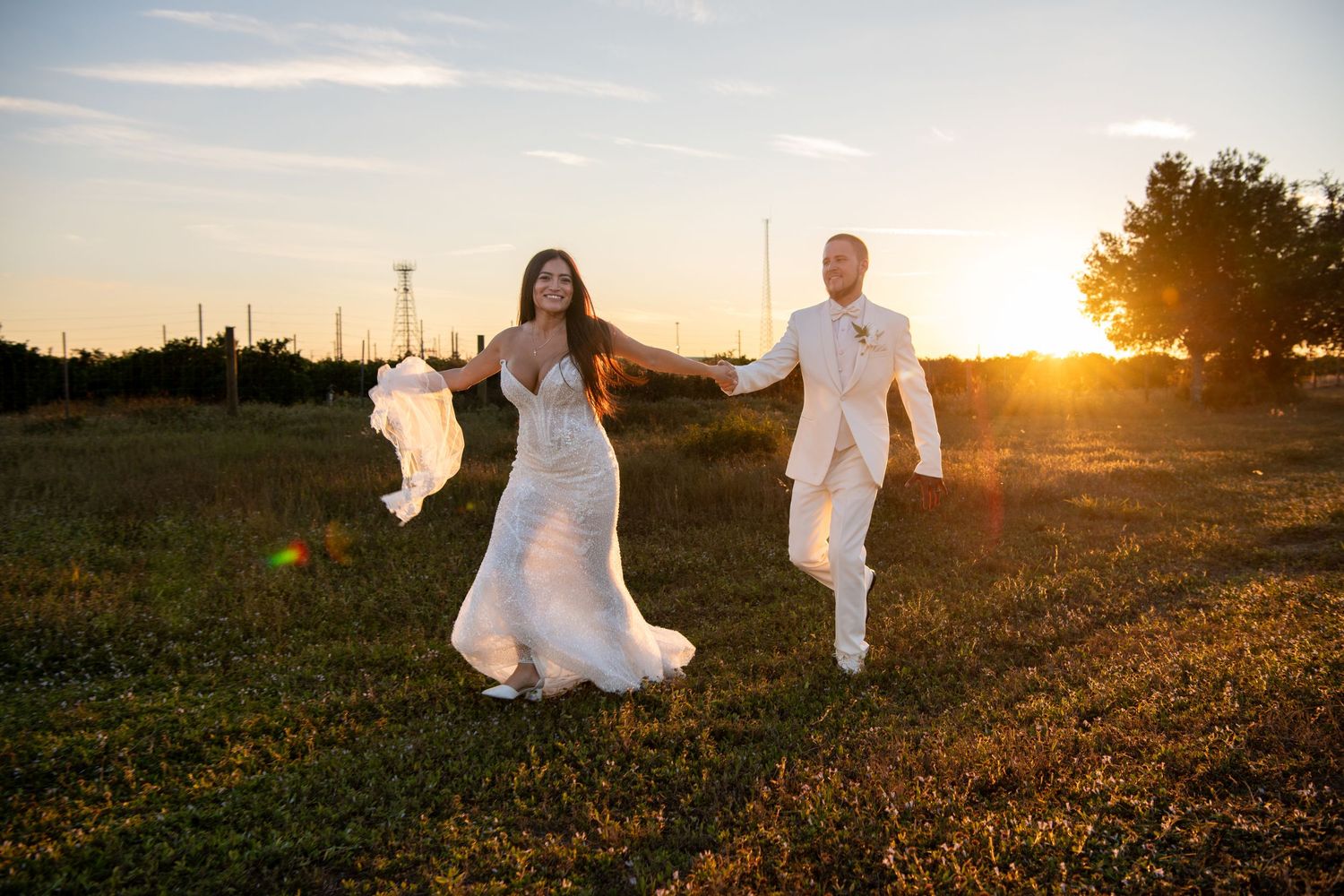 Newlyweds run and dance together in a field at sunset creating joyful candid moments. Wedding photography.
