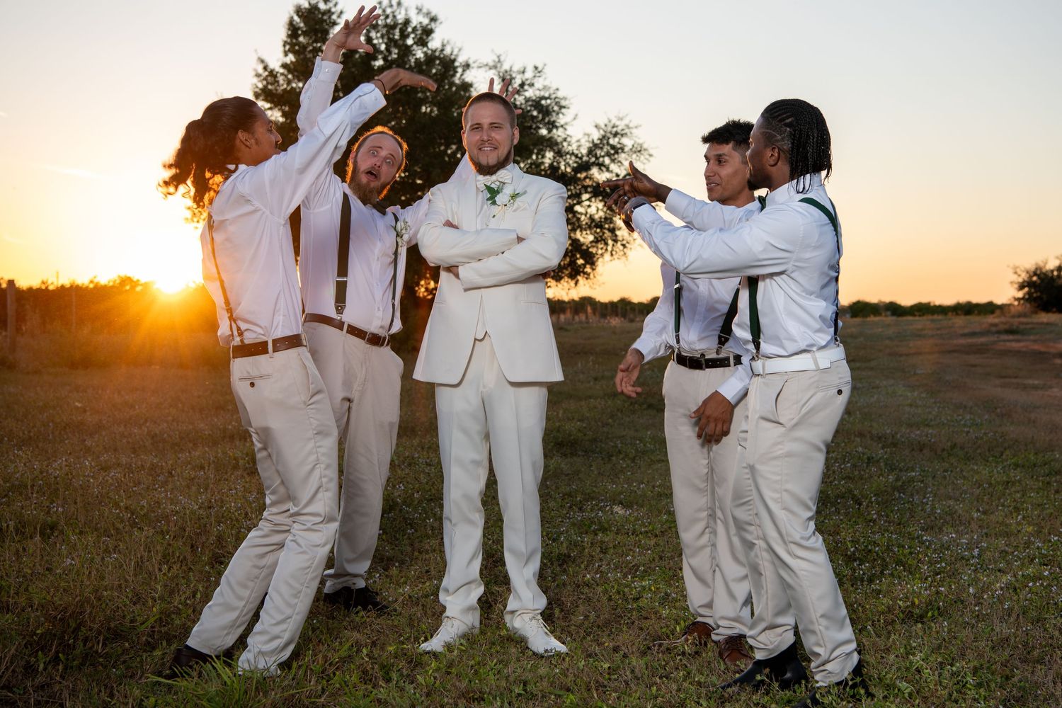 Wedding party in white attire laughs together during outdoor photo session at sunset. Wedding photography.