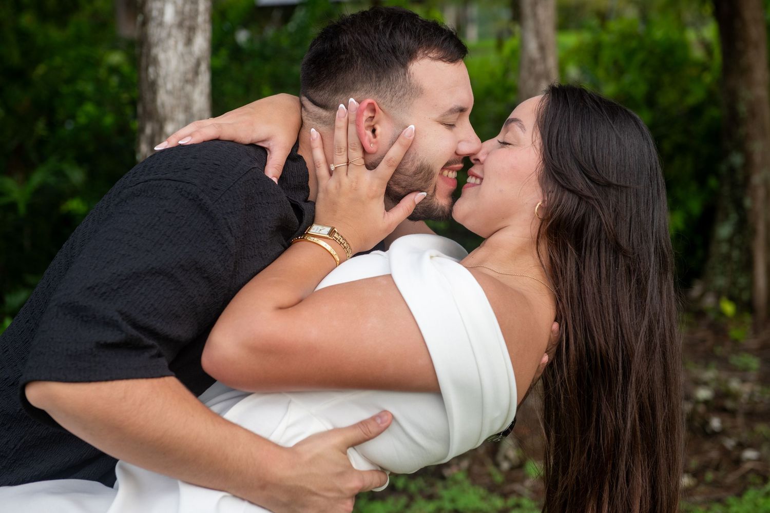 A couple shares romantic moments under hanging greenery in an outdoor setting.