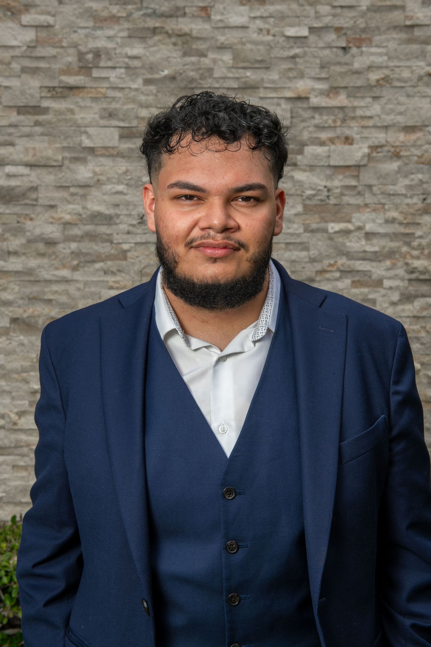 Business portrait in dark blue suit with stone wall backdrop.