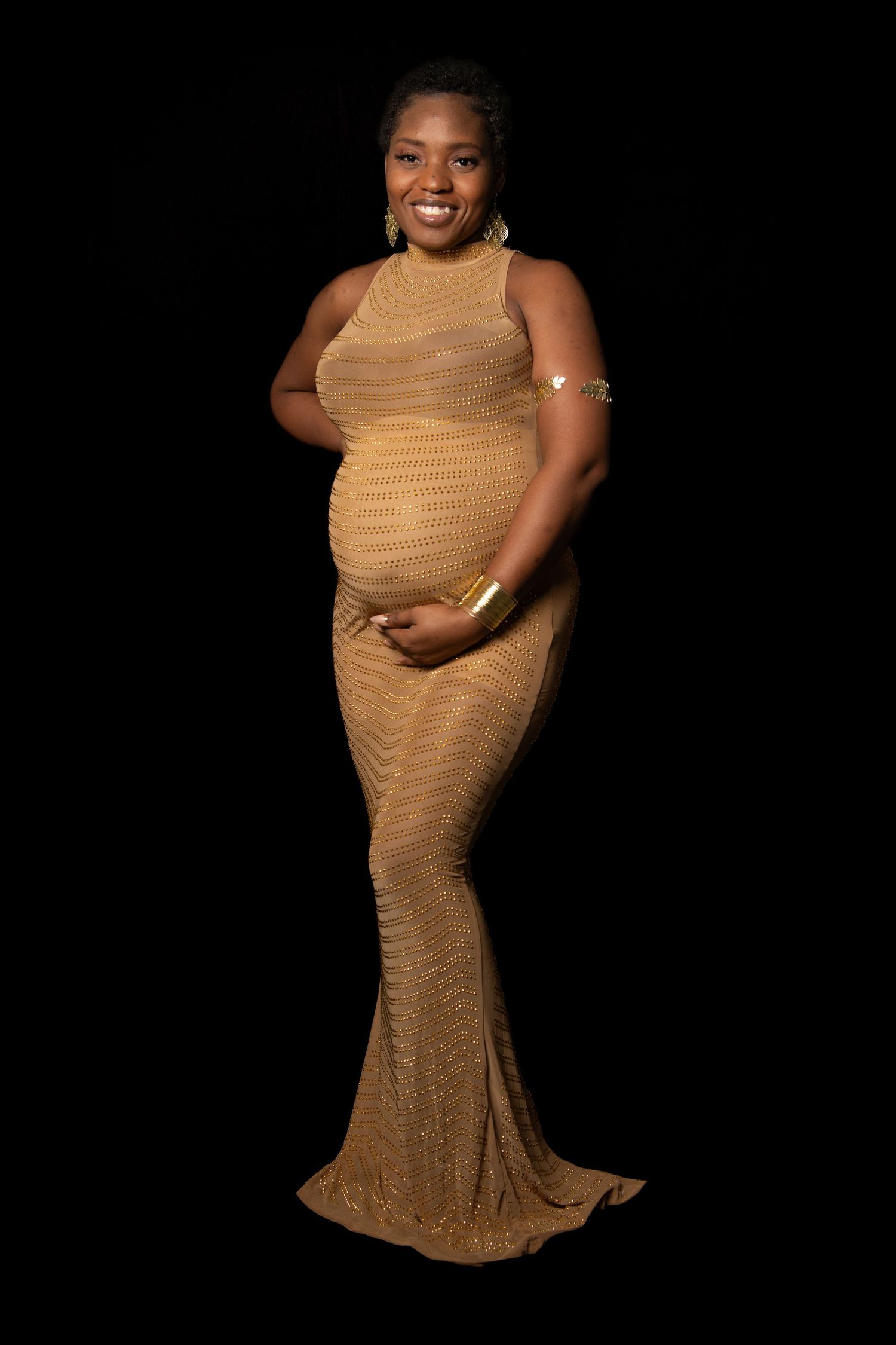 Maternity photo shoot featuring a gold knit dress against a black background. Maternity photoshoot.