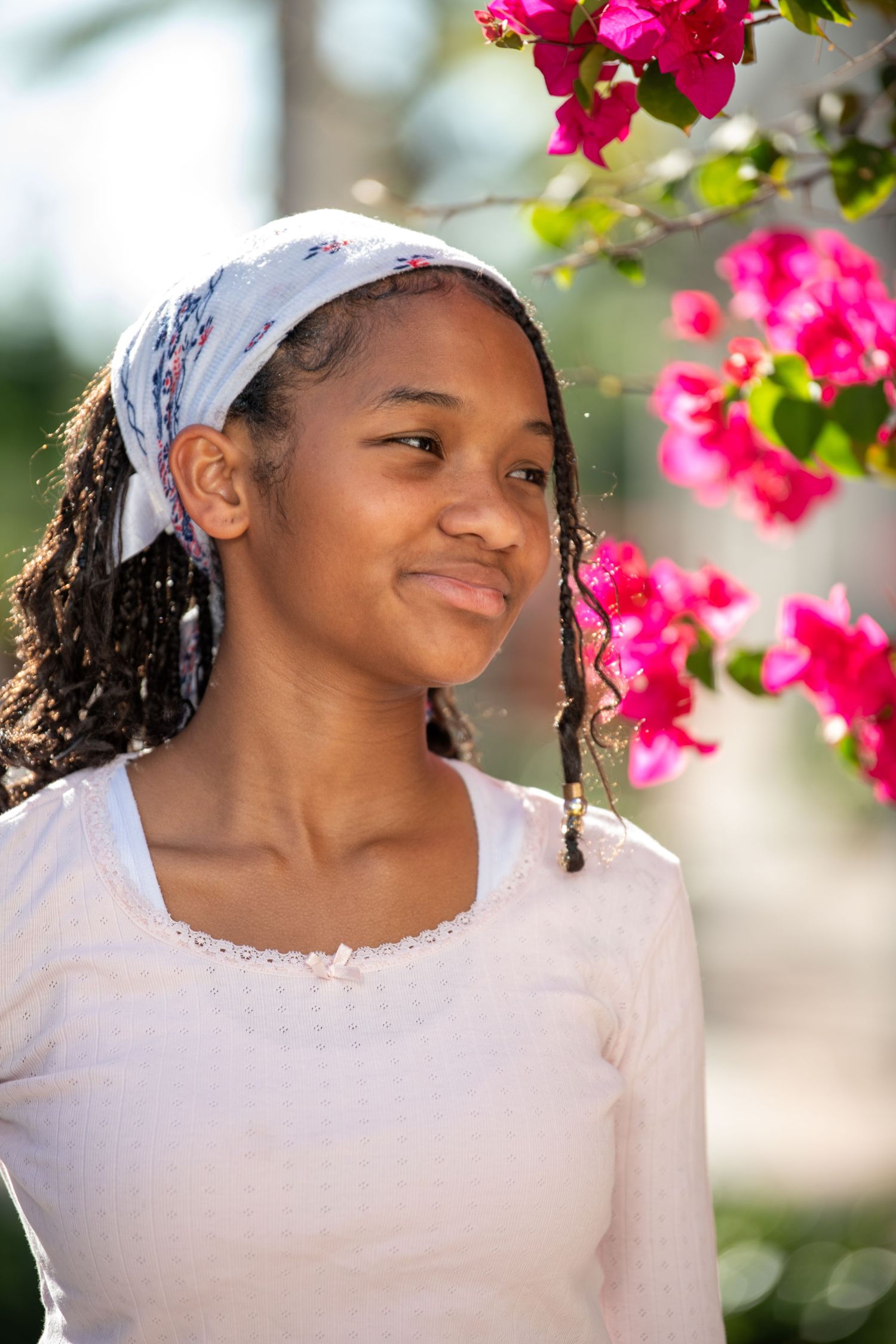 Portrait against pink bougainvillea flowers wearing white top and headscarf in natural lighting. Headshots.
