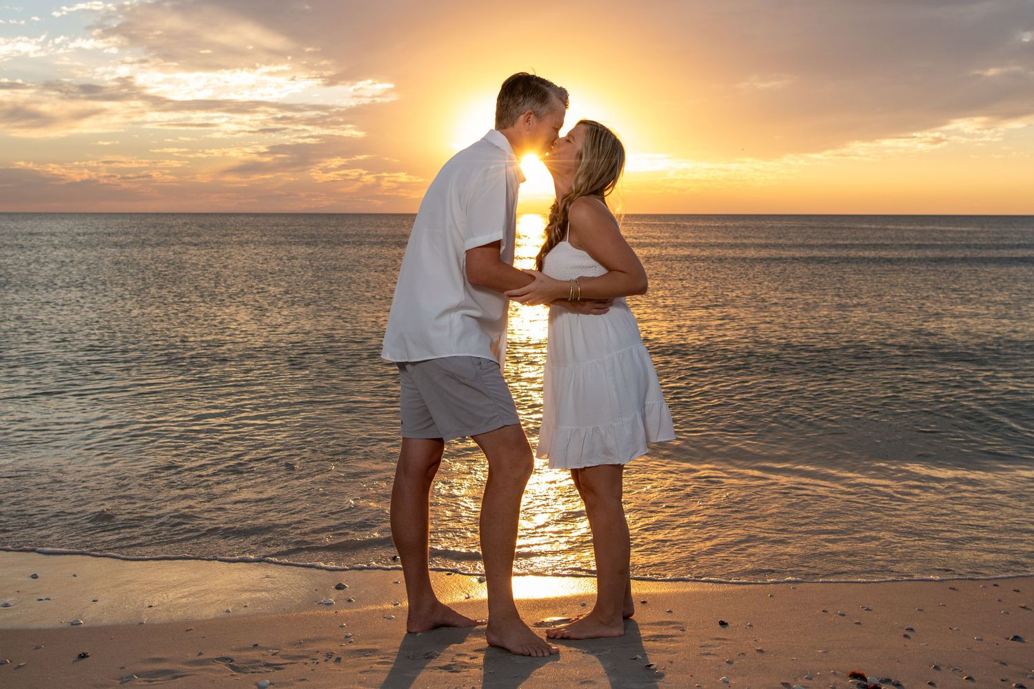 Silhouetted figures embracing on beach with brilliant orange sunset over water. Beach photoshoot. Family photoshoot,
