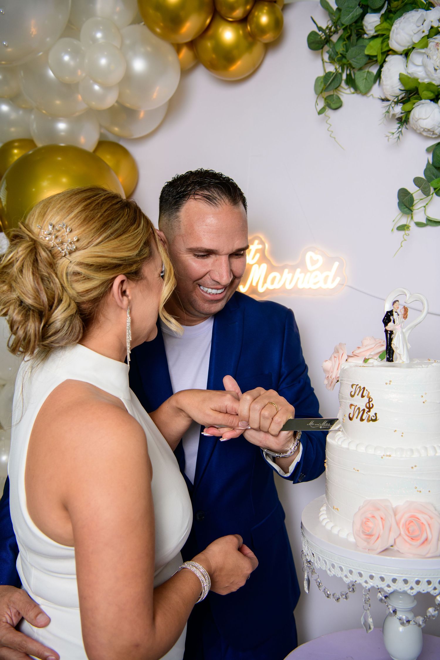 wedding portraits of Newlyweds sharing intimate moment by elegant white wedding cake with gold balloon decor.