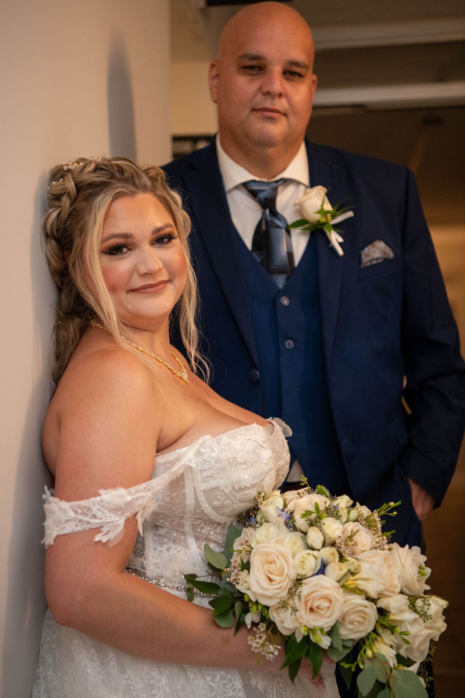 A bride holds a classic white rose bouquet while wearing an off-shoulder lace wedding gown.