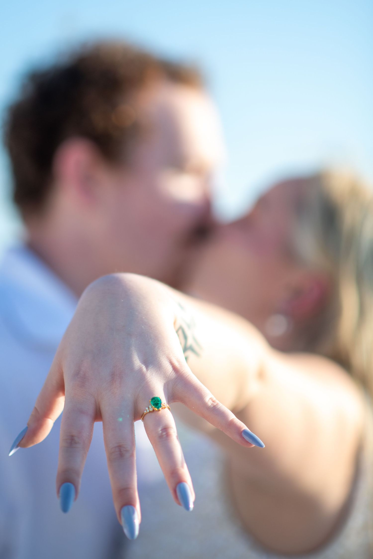 Artistic focus on engagement ring and painted nails with couple blurred in background. Engagement photoshoot. Couples photos.