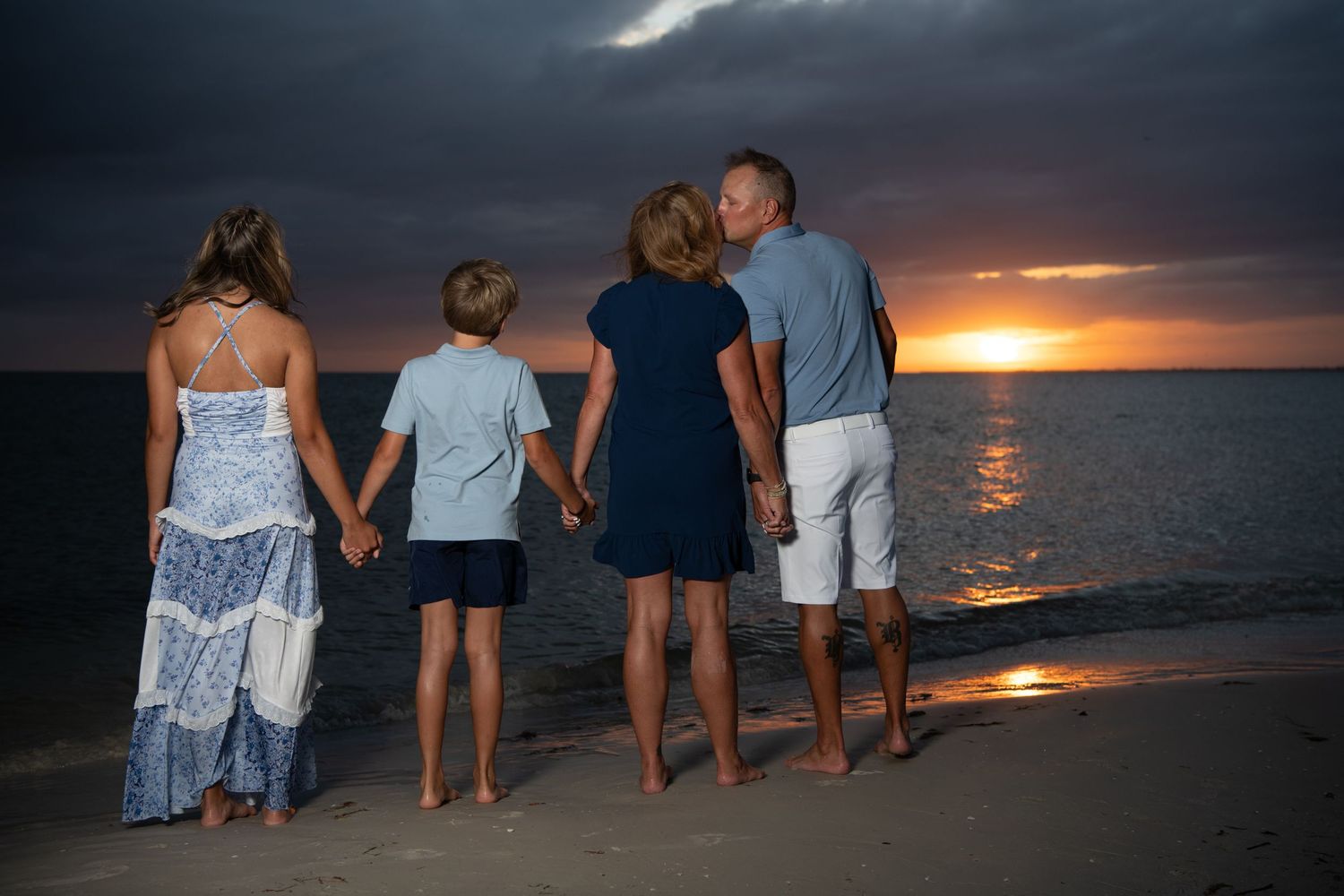 Family silhouettes walking together on beach at sunset with dramatic orange sky and ocean waves. Beach photoshoot. Family photoshoot,