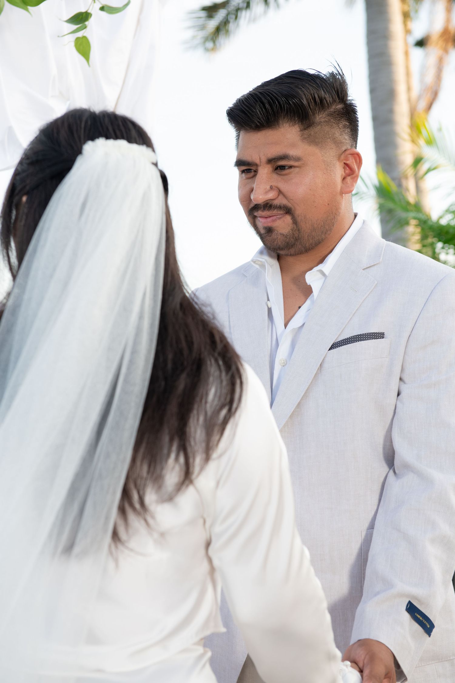 Wedding couple in all white attire sharing tender moments outdoors.