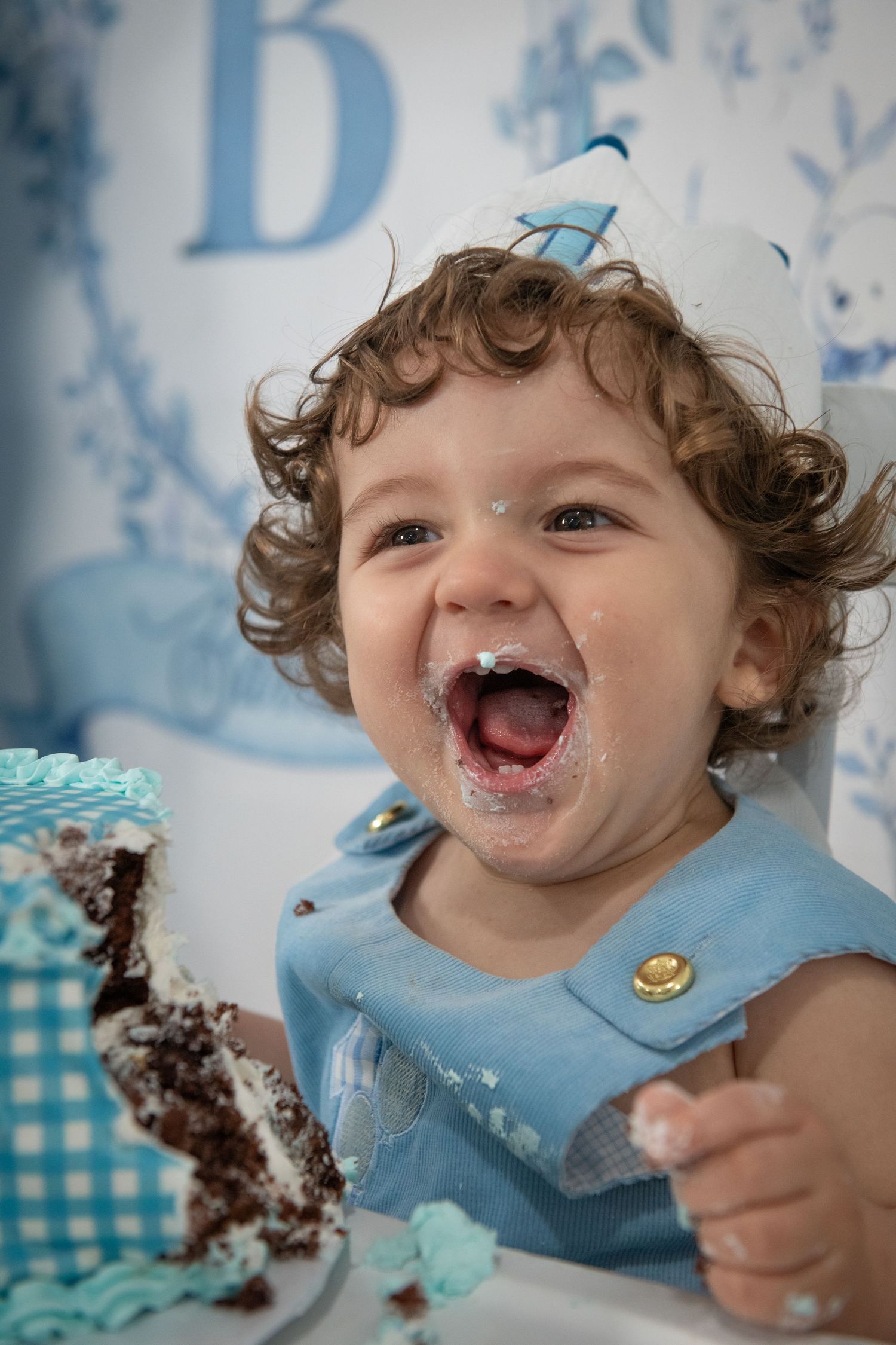 Toddler with chocolate cake smeared on face laughs during cake smash photo session.