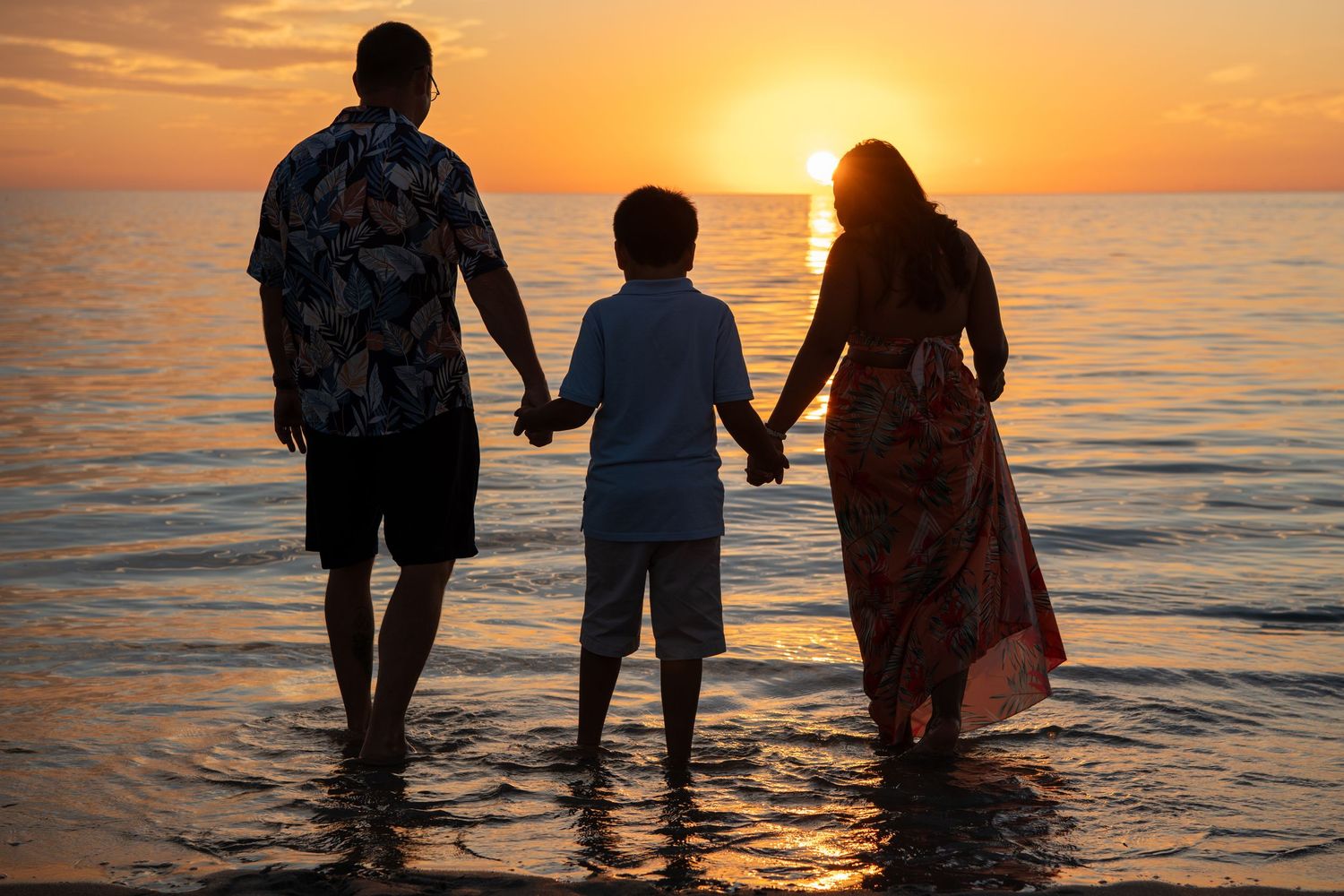 Silhouettes holding hands while standing in ocean water during dramatic sunset. Beach photoshoot. Family photoshoot,