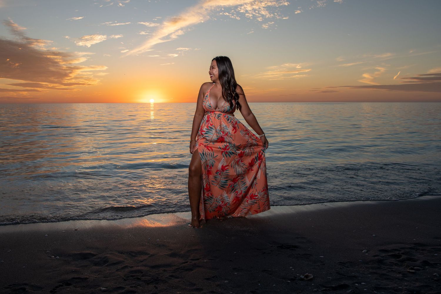 Woman in floral maxi dress poses on beach during golden hour sunset. Beach photoshoot.