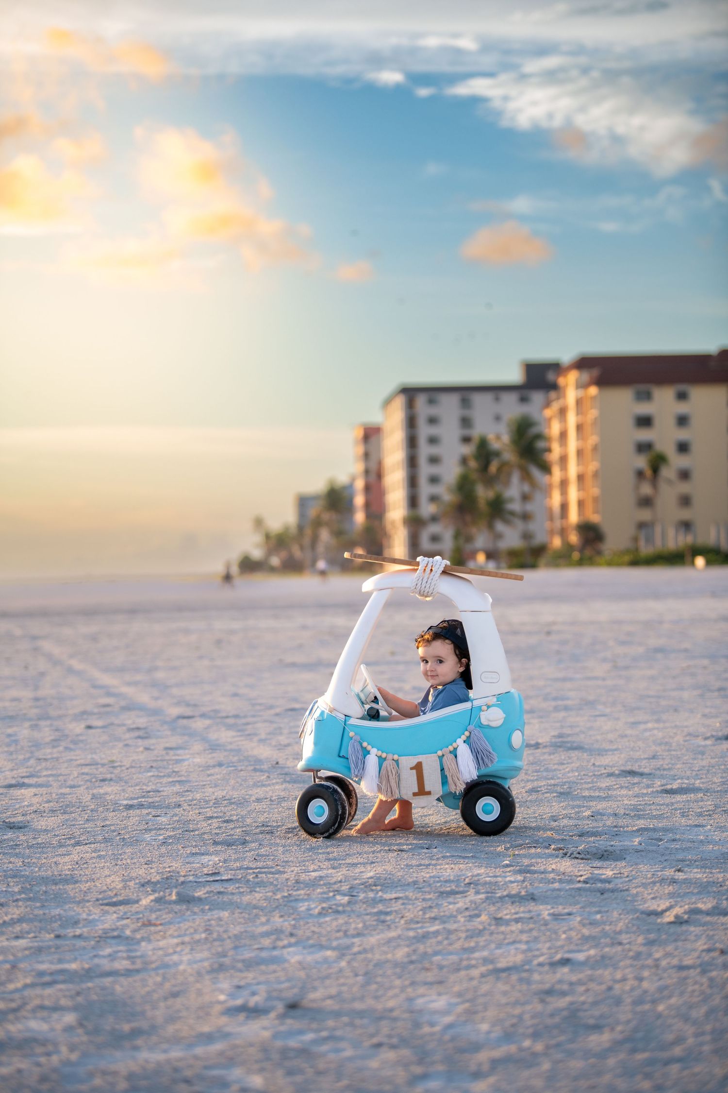 Light blue toy scooter on sandy beach with coastal buildings in background.