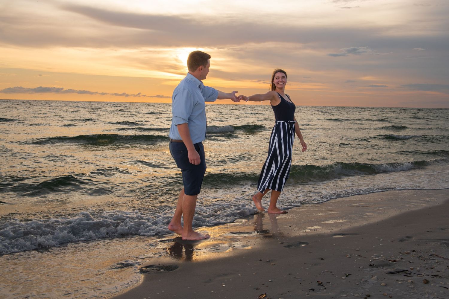 People strolling along the shoreline during a dramatic beach sunset with waves crashing nearby.