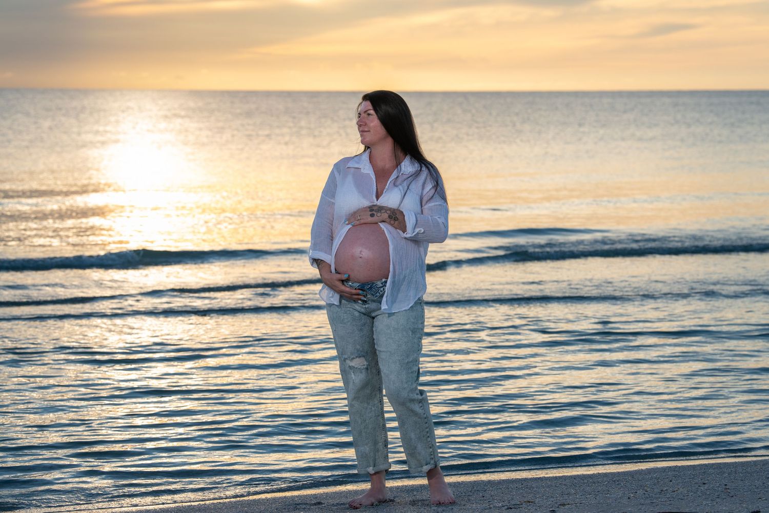 Couple sharing intimate moment on beach during golden hour. Maternity photoshoot.