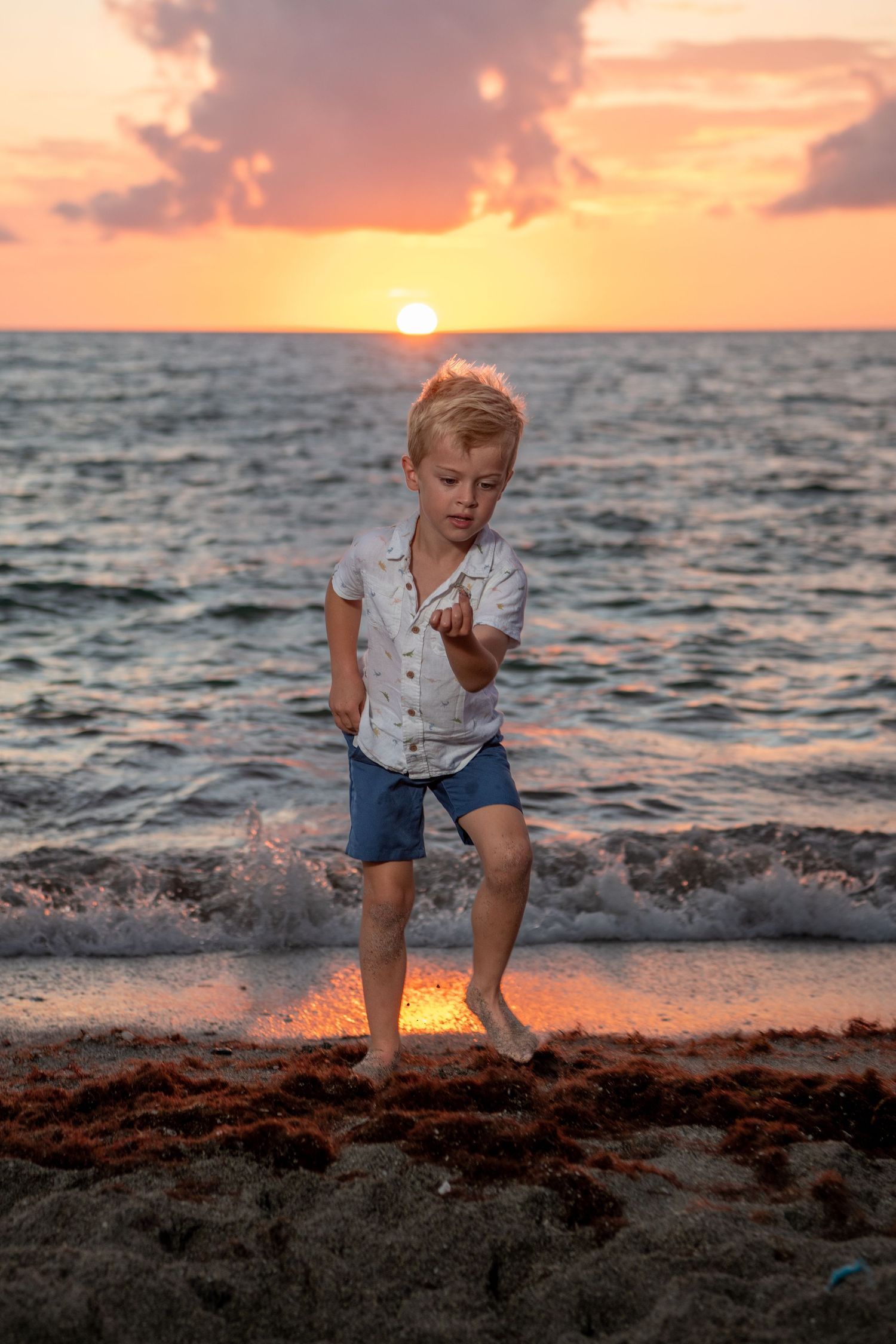 Young child playing on sandy beach during a vibrant orange sunset. Beach photoshoot.