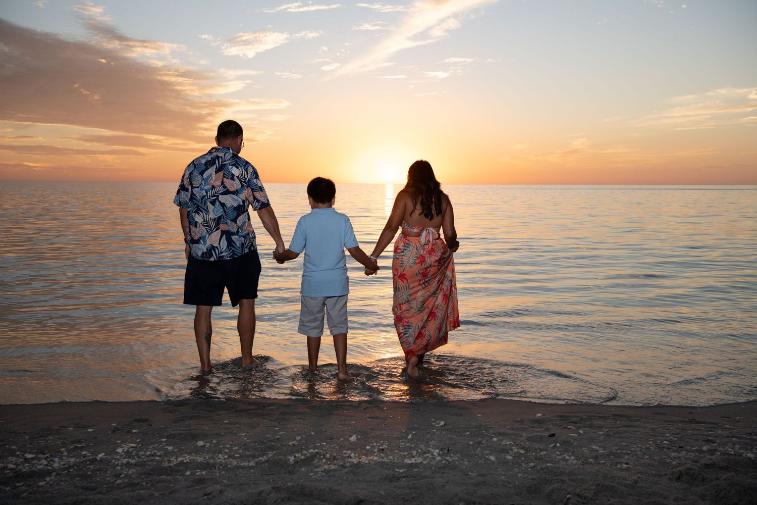 Three people standing in shallow ocean water watching sunset together. Beach photoshoot. Family photoshoot,