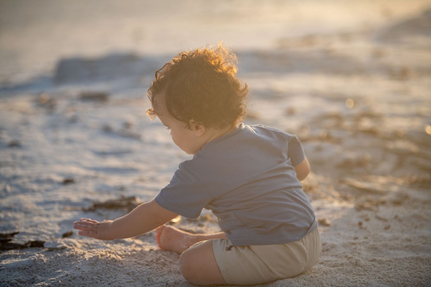 Silhouette of child playing in sand during golden hour at beach.