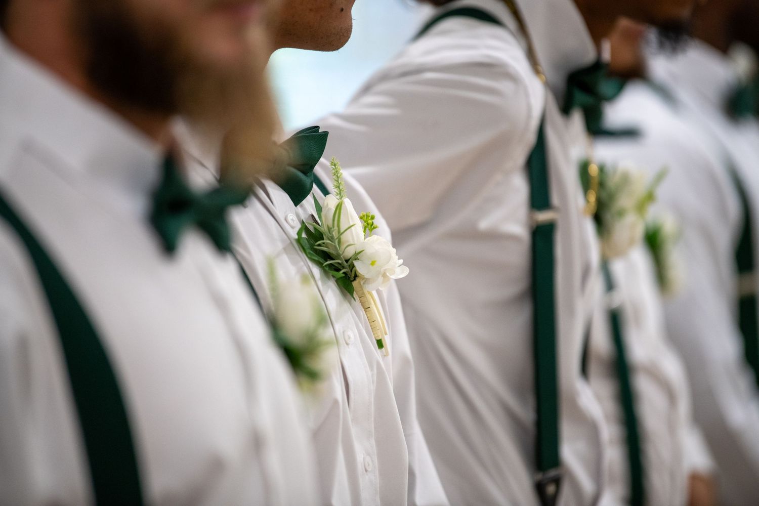 Wedding party members in crisp white suits with green accents stand together. Wedding photography.