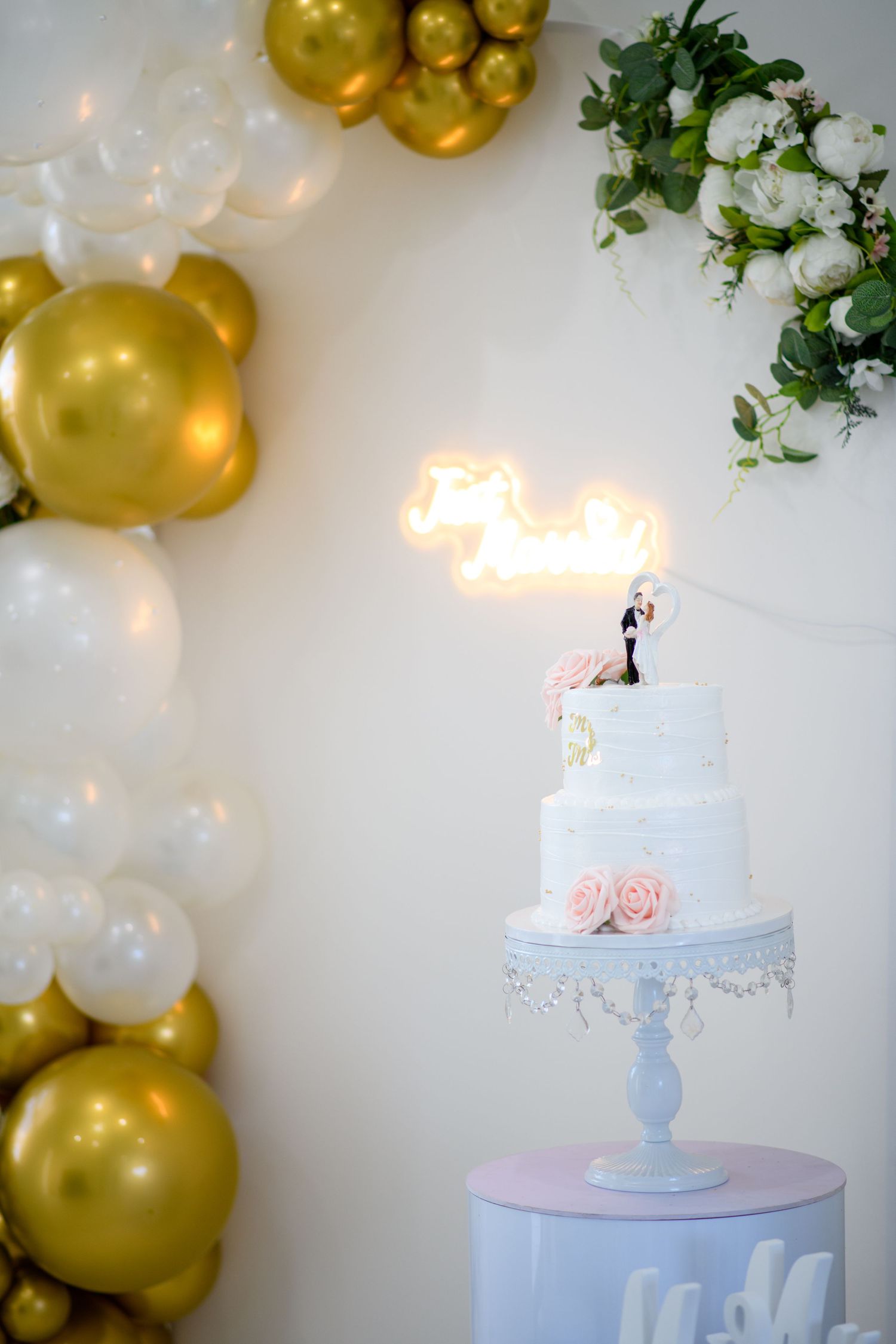 Wedding cake display with gold and white balloon decorations and floral accents.