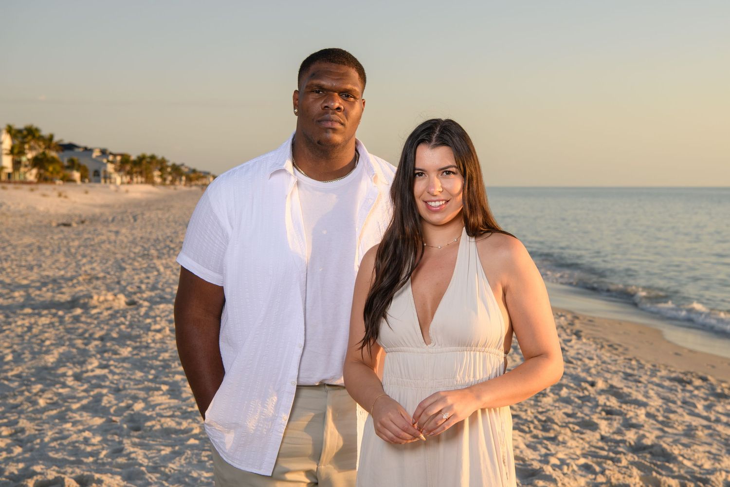 Couple in coordinated white outfits posing for beach photos. Engagement photoshoot. Couples photos.