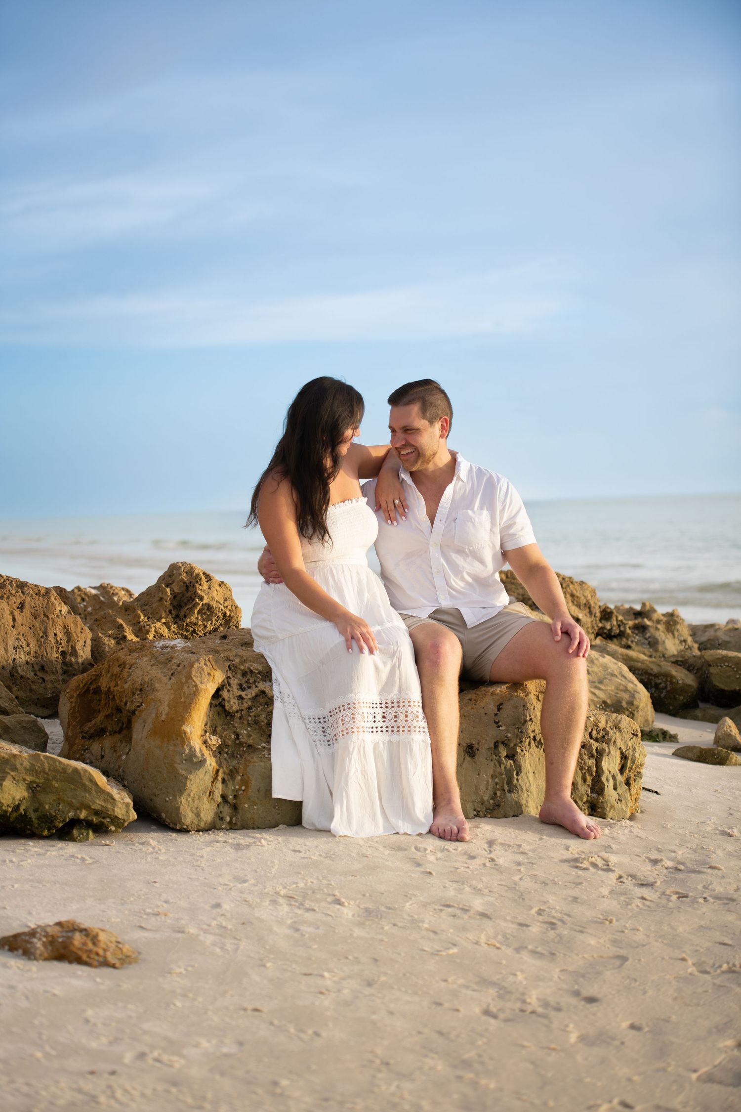 Romantic beach portraits with couple posed on rocky shoreline.