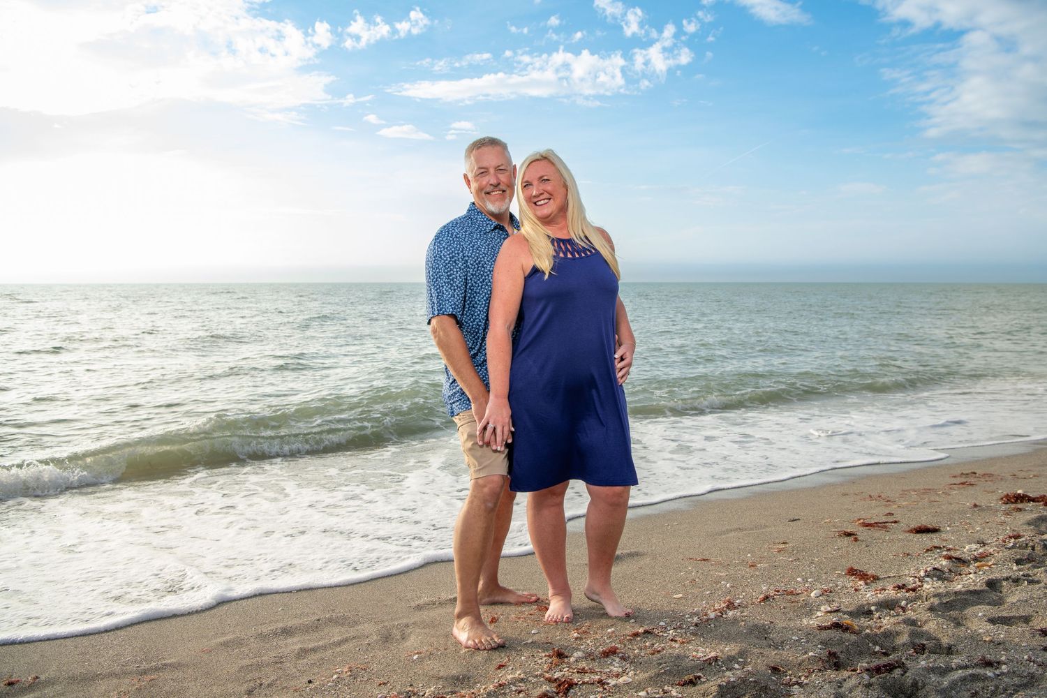 A couple poses together on a beach at sunset with ocean waves in the background. Family photoshoot.