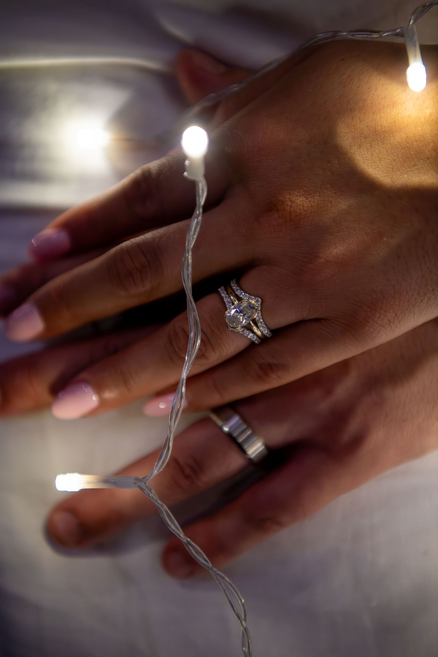 Close-up of hands with engagement ring illuminated by string lights. Wedding photography.