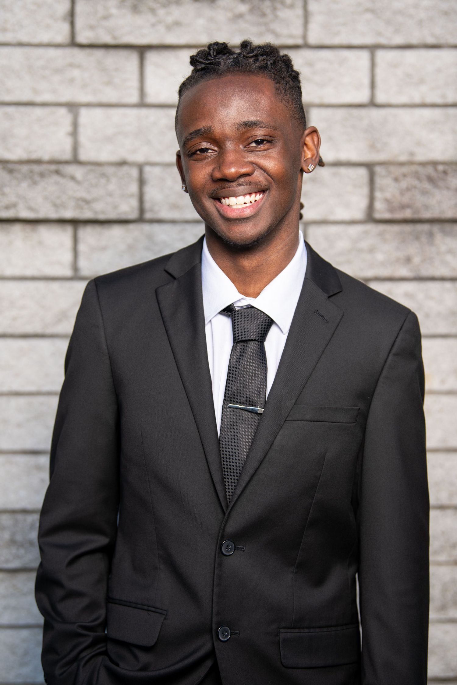 Professional headshots of a person in a black suit and tie against a white brick background. Professional headshots. Self portraits.