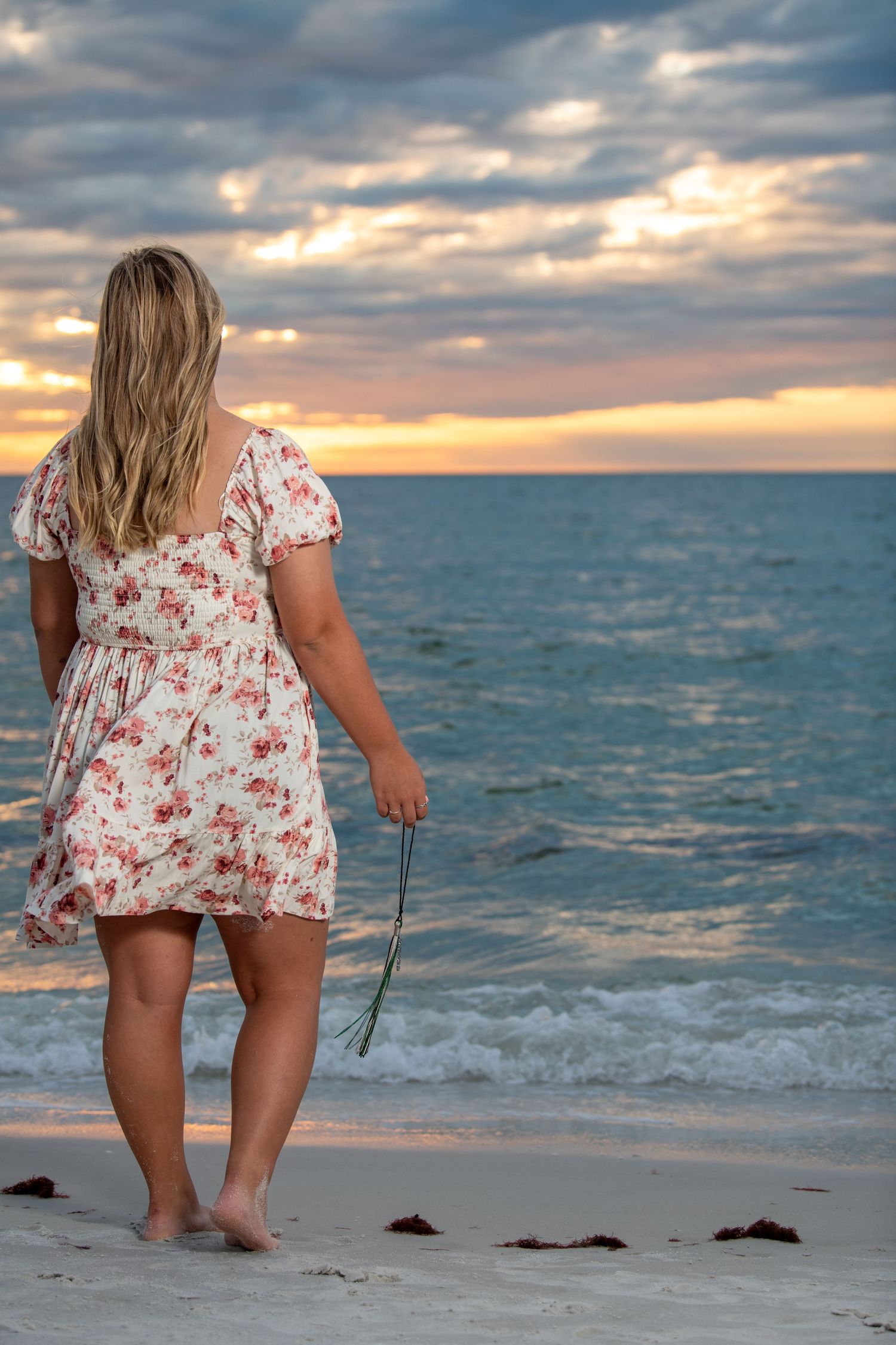 Person in floral dress walking along beach shore during golden hour sunset. Self portraits. Senior photos.