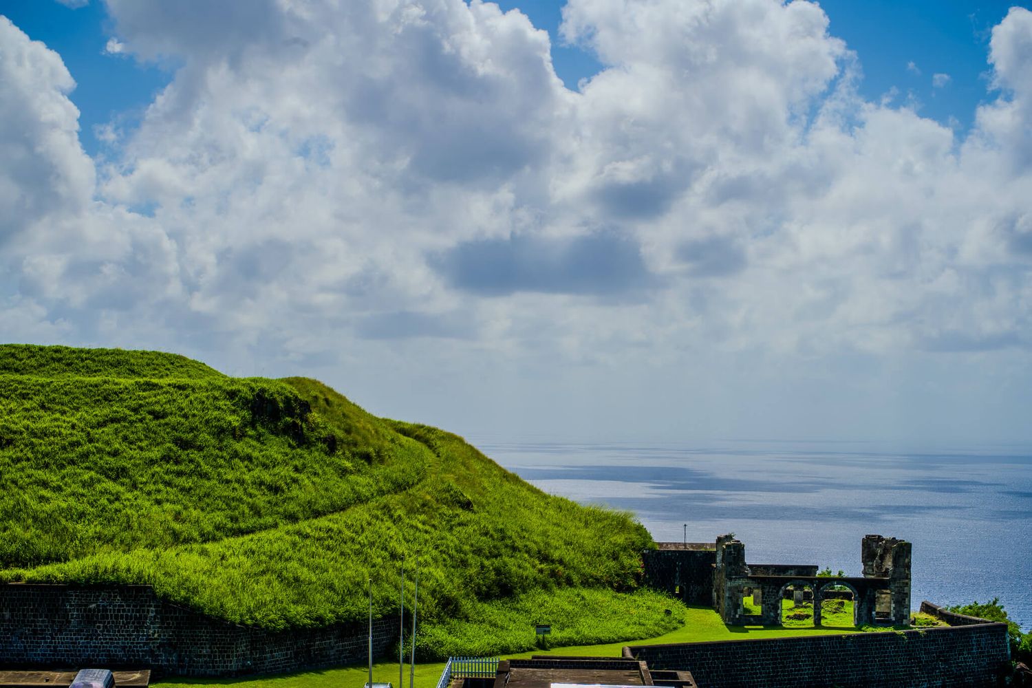 Panoramic view of green cliffs along the rugged coastline from Brimstone Hill in St. Kitts under cloudy blue skies.