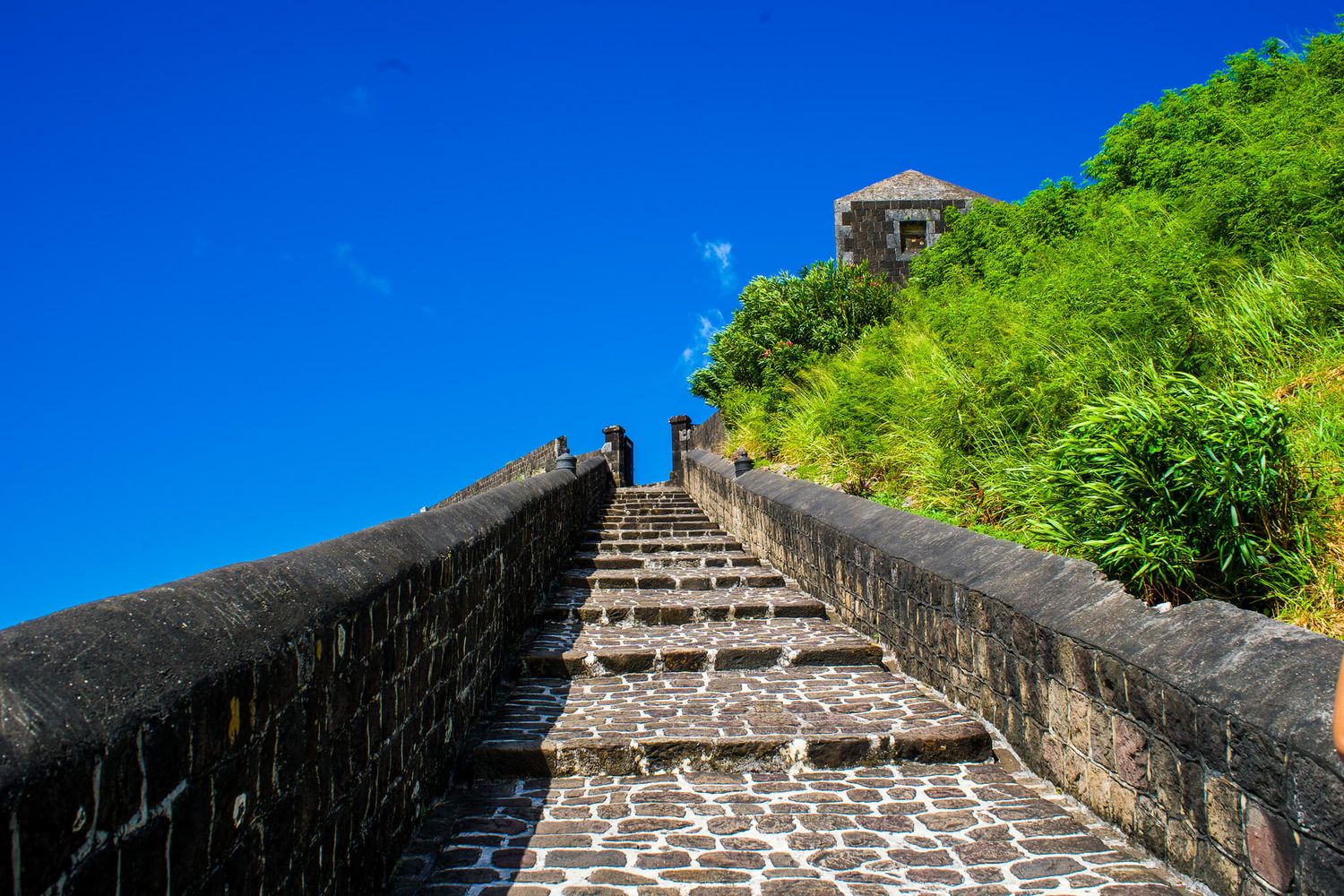 Aerial view of the Great Wall of China winding through lush green mountains under bright blue sky.