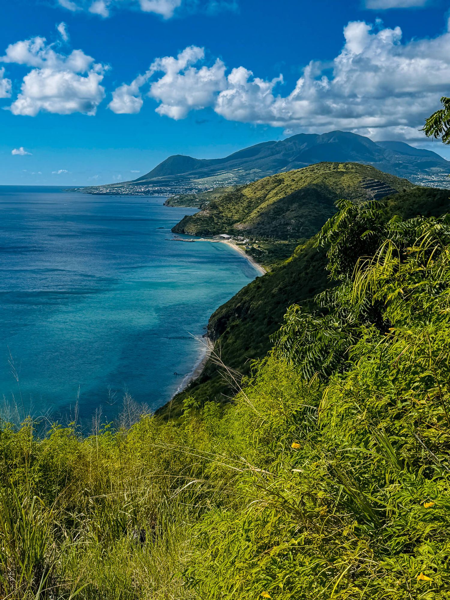 Panoramic coastal view of Saint Kitts island with lush green mountains and turquoise Caribbean waters. Stop here on the best St. Kitts Tours