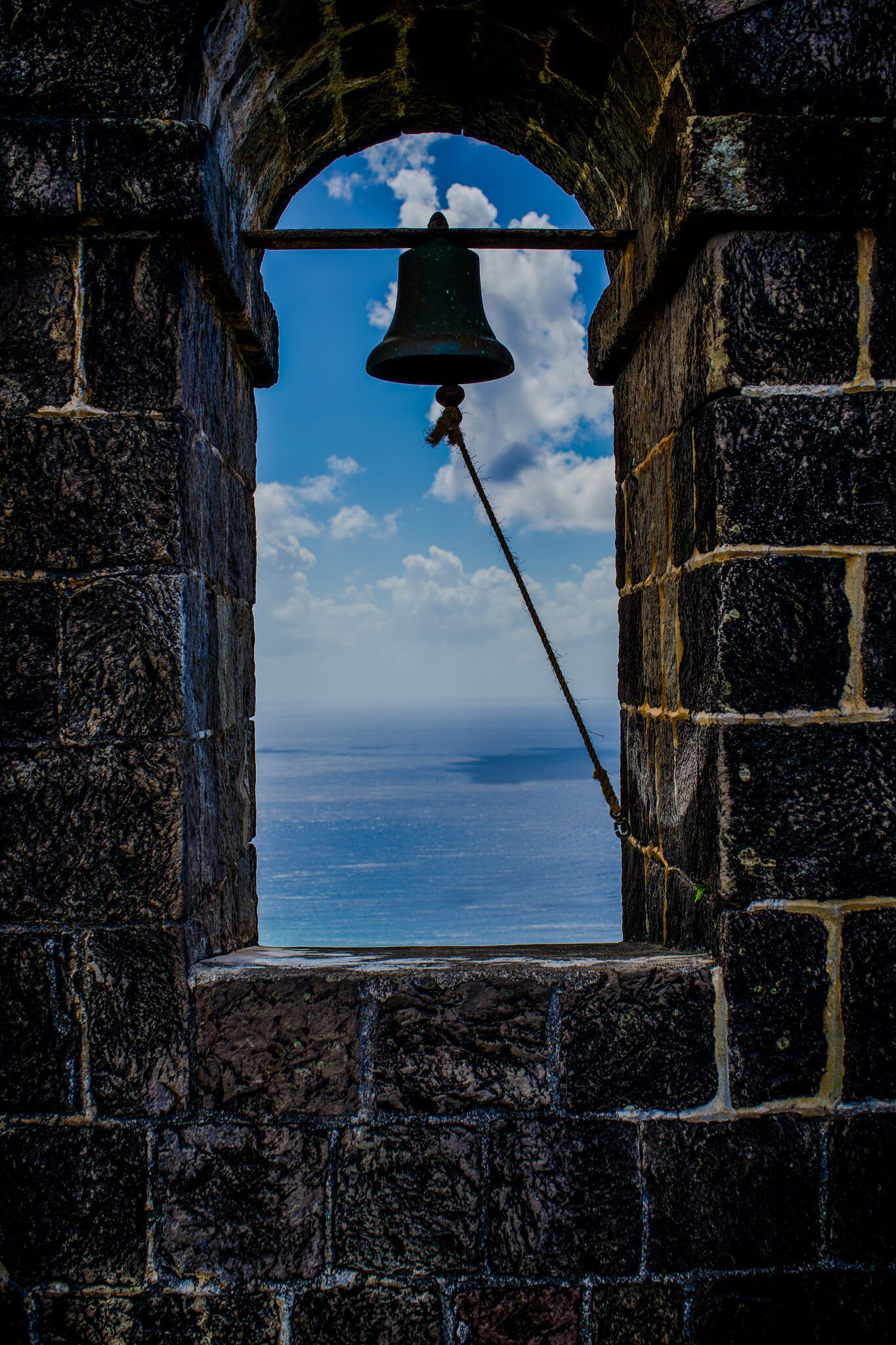 Stone fortress window frames a stunning view of the blue Caribbean Sea and sky with puffy white clouds on the horizon.