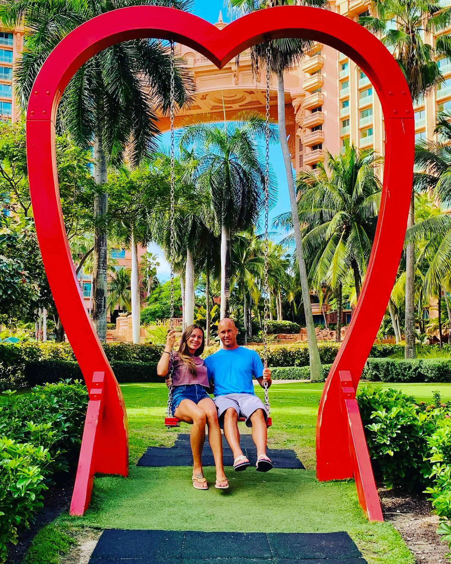 Large red heart-shaped arches create a romantic walkway in a tropical garden setting.