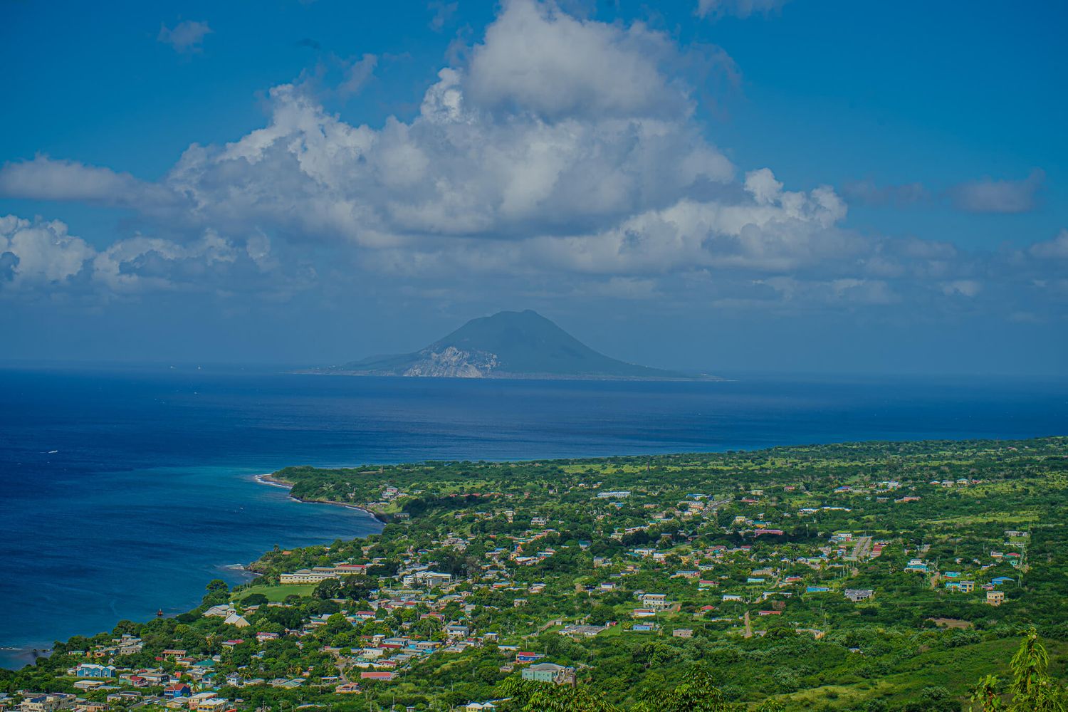 Panoramic aerial view of a lush Caribbean coastline from Brimstone Hill in St. Kitts with views of turquoise waters and Saba island.