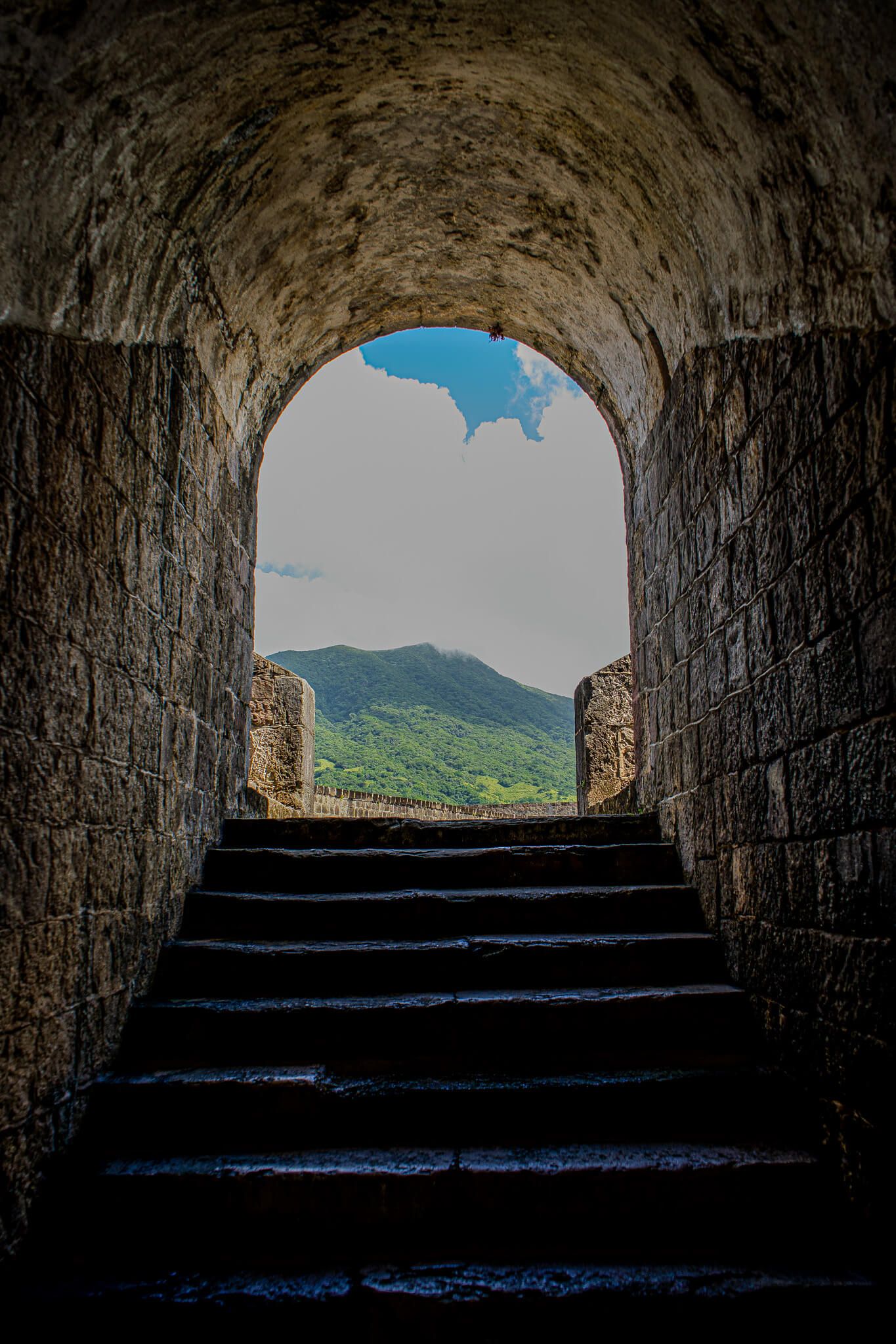 Stone tunnel entrance with steps reveals scenic mountain views through a series of arched openings.