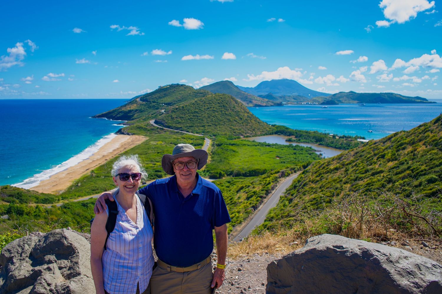 Two tourists enjoy scenic views of turquoise waters and green hills at Timothy HIll. Stop here on the best St. Kitts Tours.