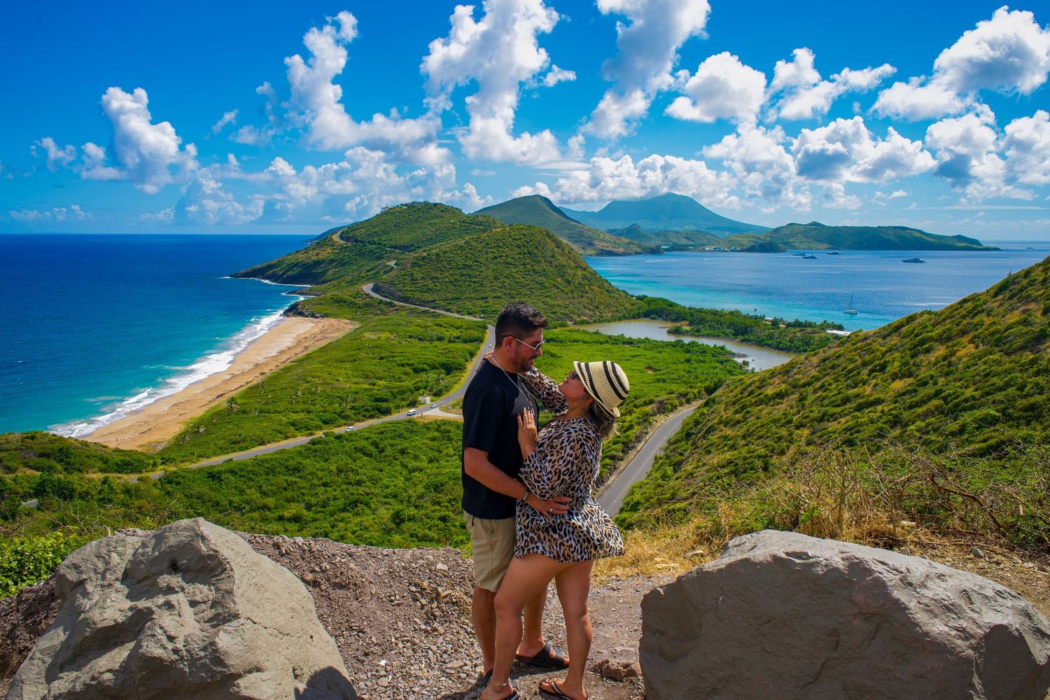 Couple enjoying scenic overlook of turquoise waters and green hills at Timothy Hill in Saint Kitts. Stop here on the best St. Kitts Tours.