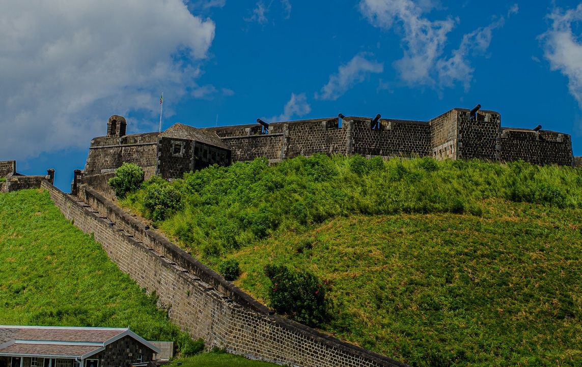 Ancient stone walls of the Great Wall of China stretch across lush green hills under a bright blue summer sky.