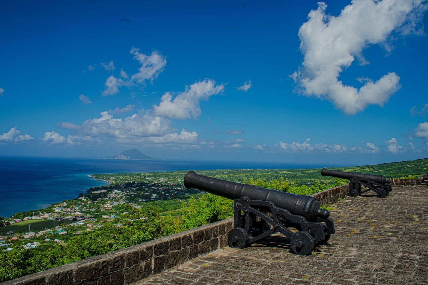 Panoramic view of a historic stone fortress wall in Brimstone Hill in St. Kitts overlooking a tropical coastline.