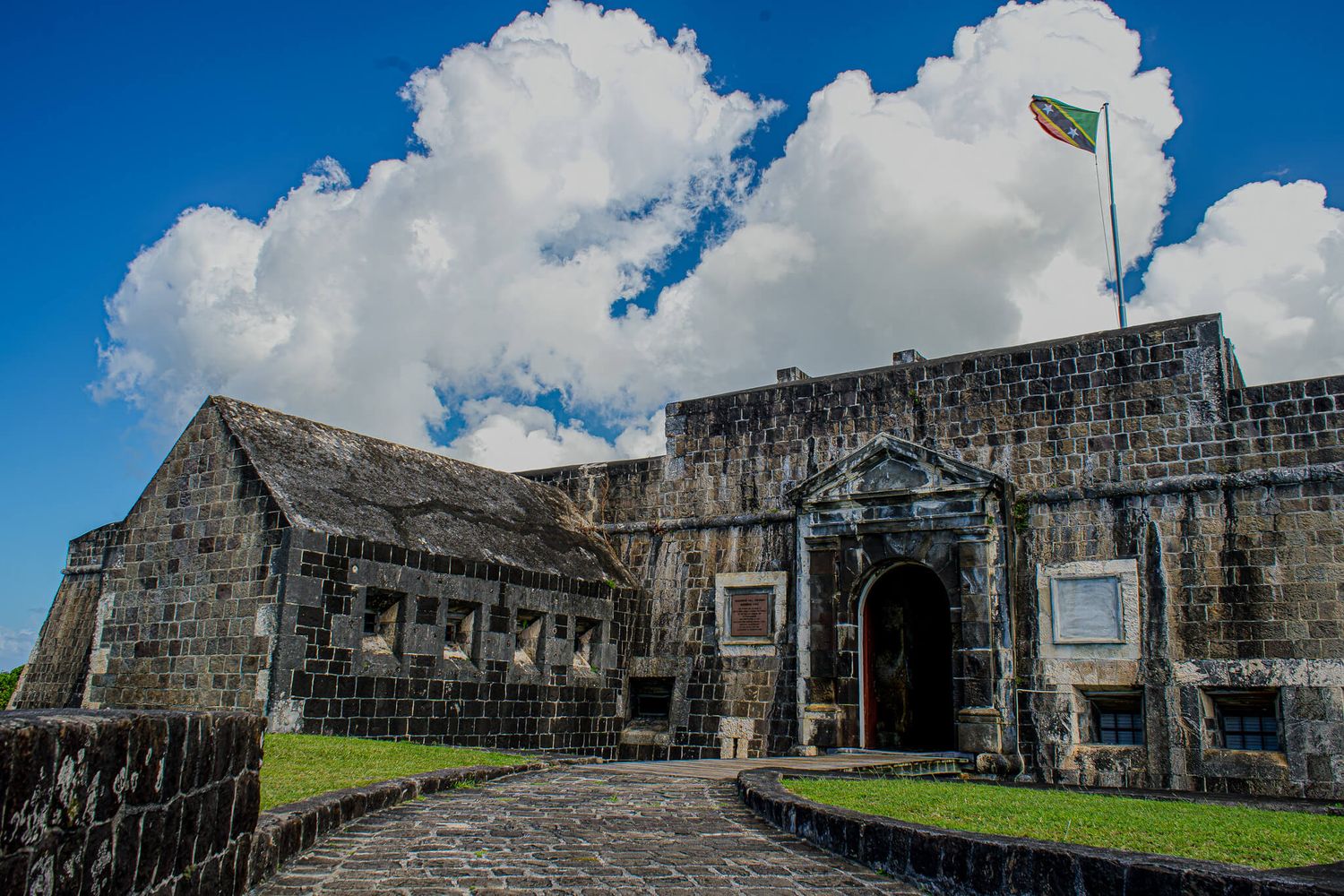 Ancient stone fortress walls stretch along a hilltop under puffy white clouds and bright blue sky.