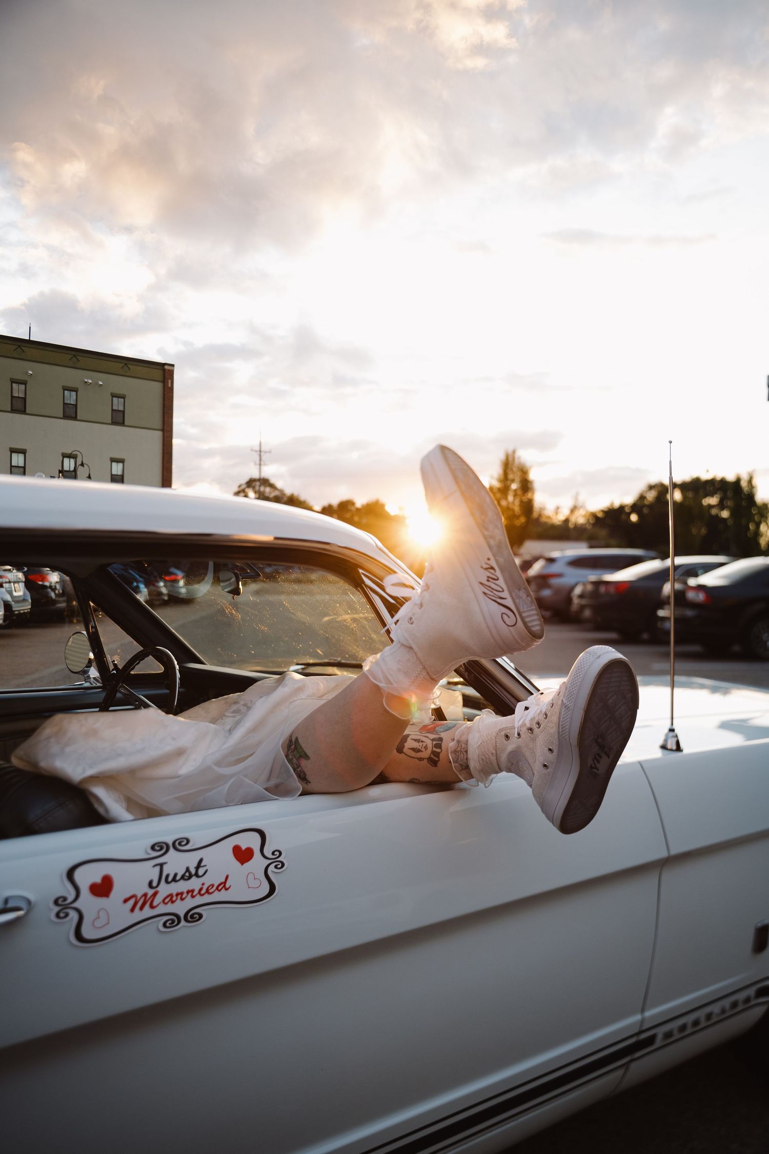 White vintage convertible car with 'Just Married' text parked during golden hour sunset.