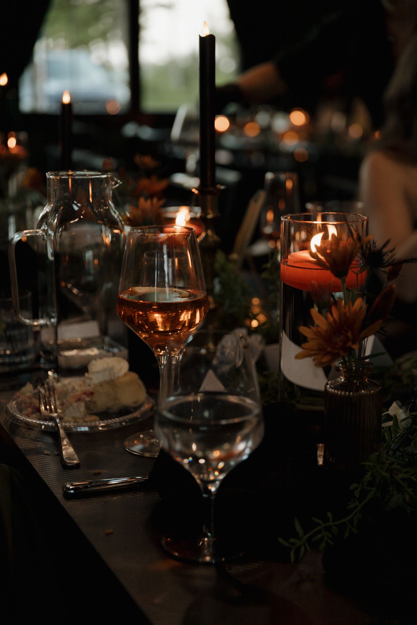 Moody wedding reception table setting with candlelight and wine glasses in dark ambient lighting.