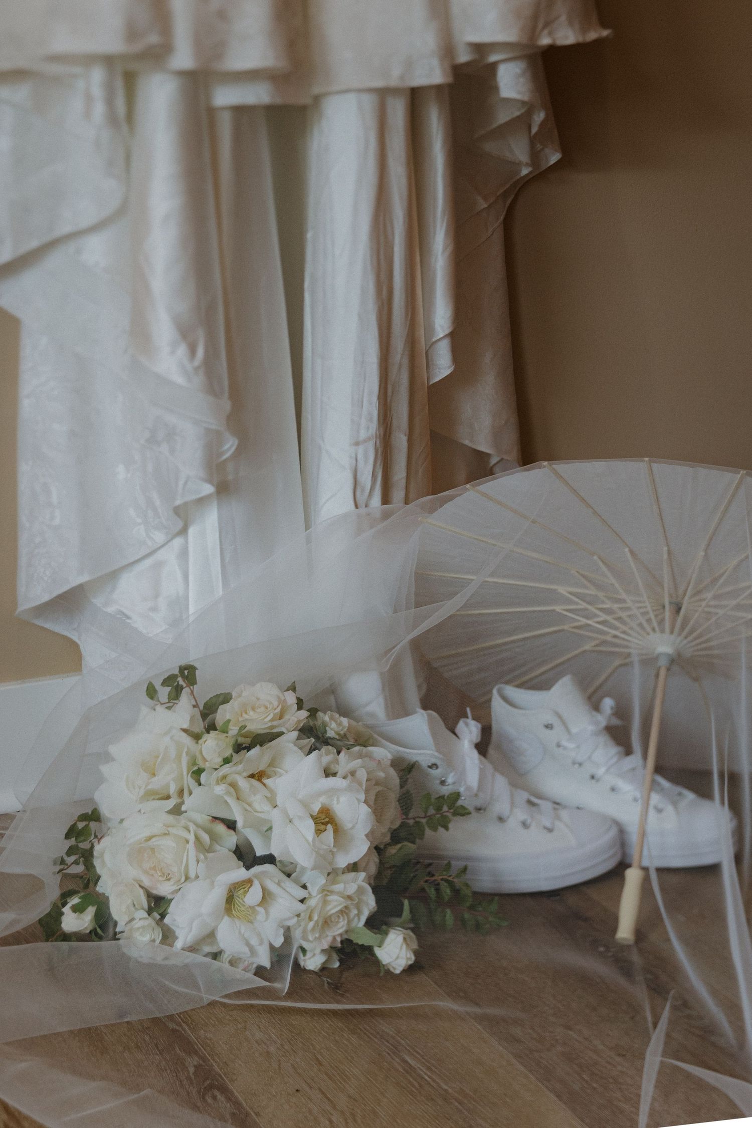 White wedding dresses hang beside delicate floral arrangements and parasols in a soft, romantic bridal setting.