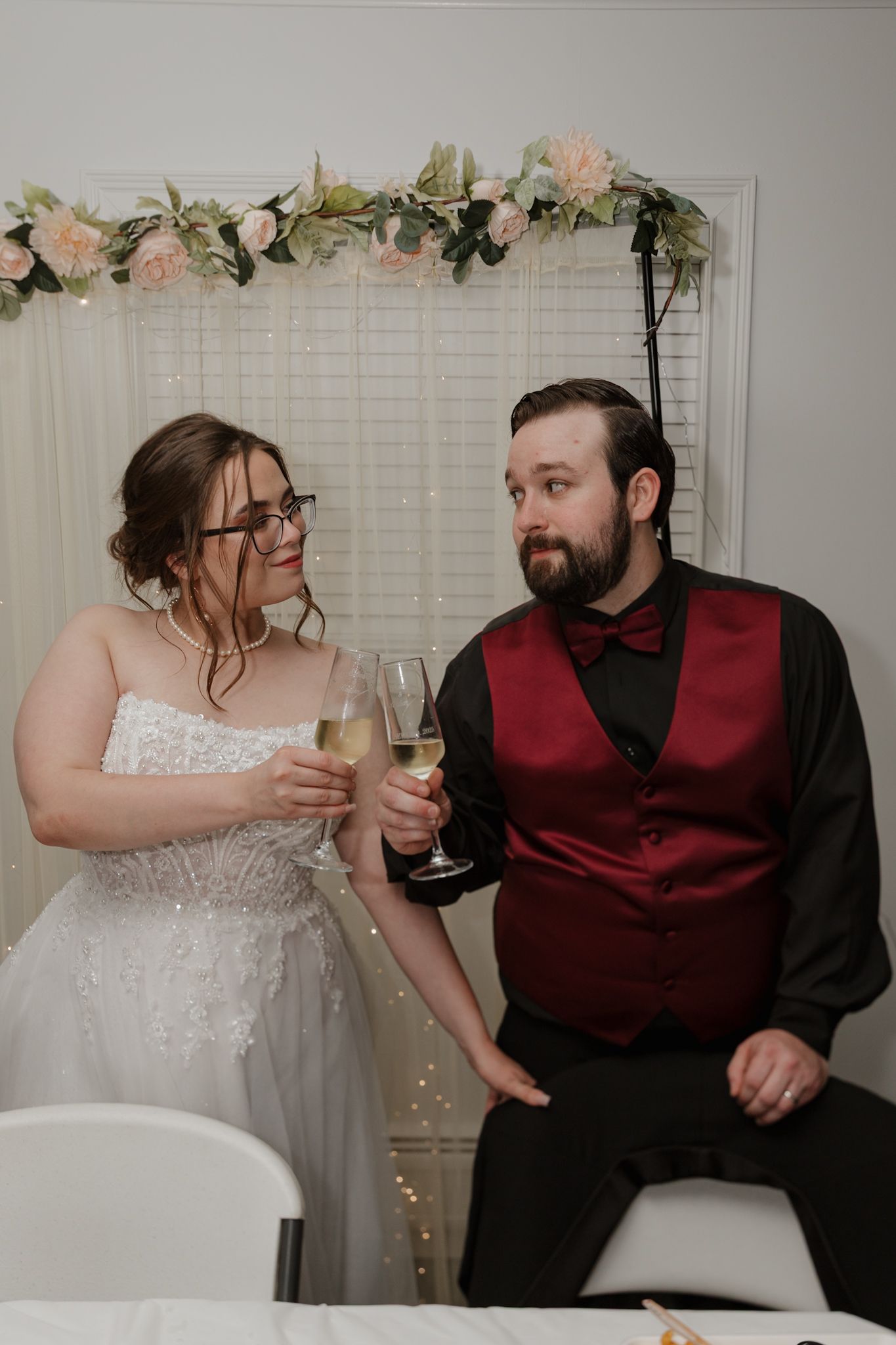 A couple in wedding attire shares playful moments while holding champagne glasses during their intimate celebration.