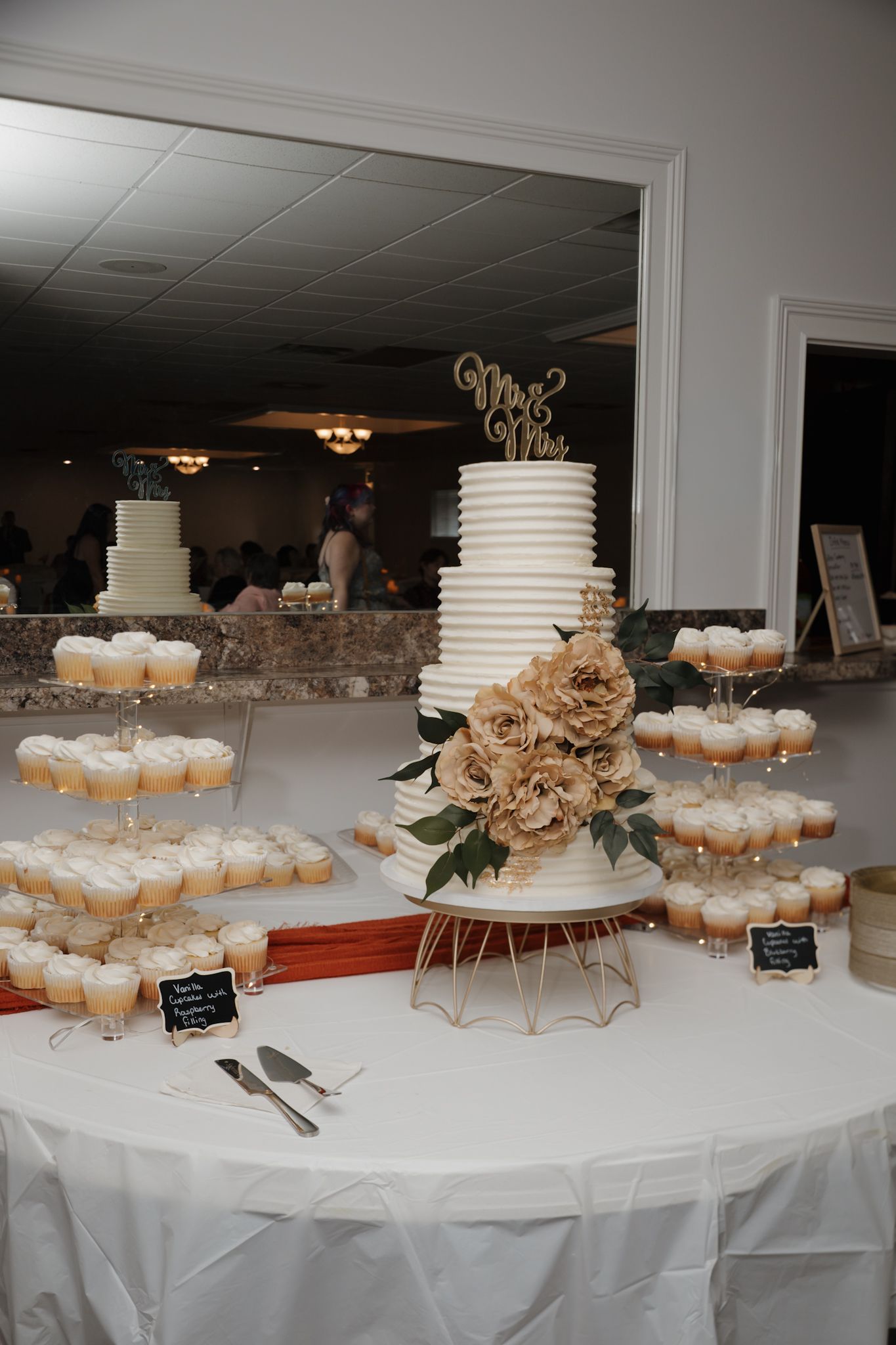 Wedding dessert table with tiered white cakes and cupcakes arranged on elegant stands with burlap decorations.
