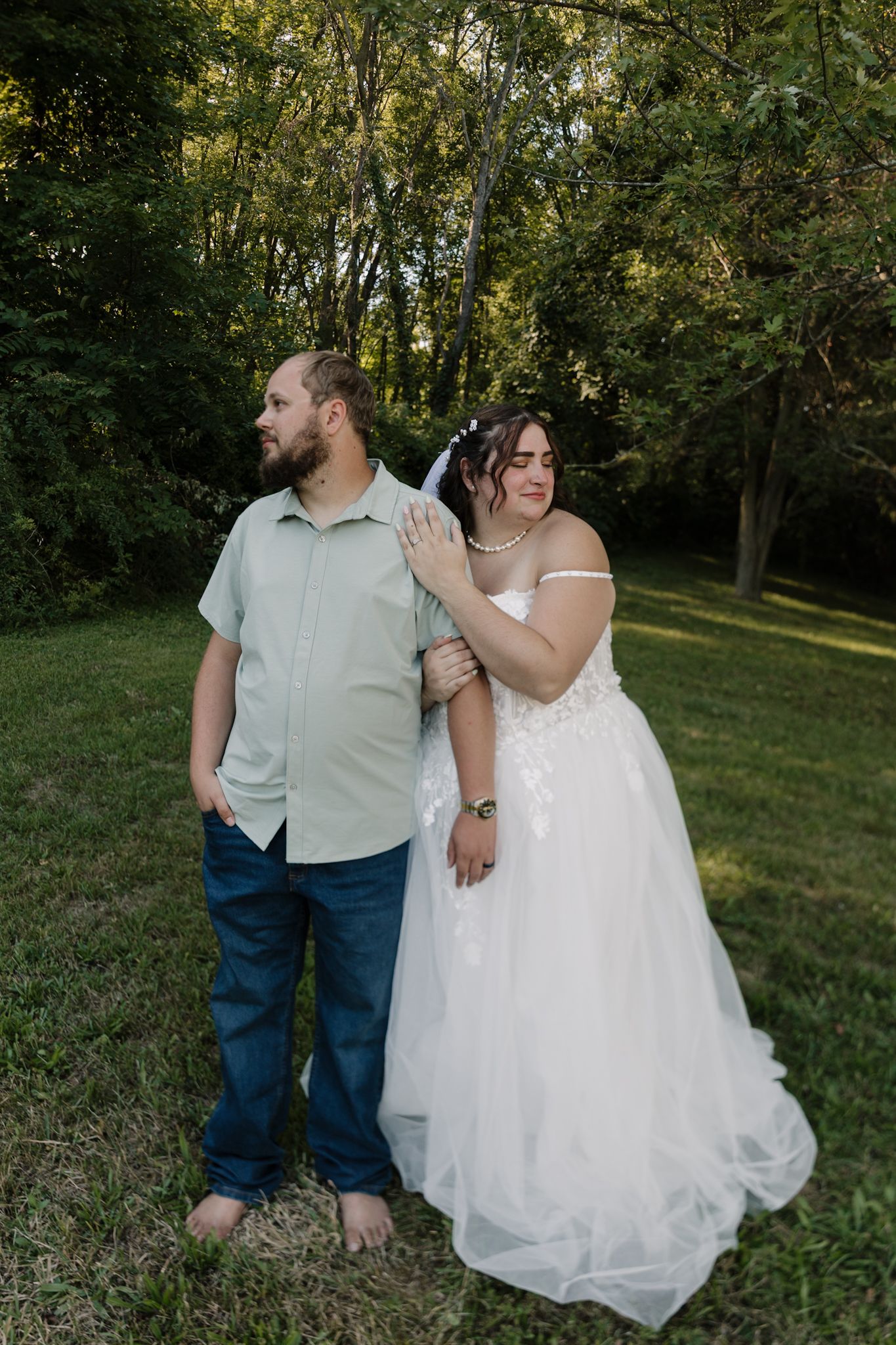 A couple sits together outdoors in a wooded area during a romantic wedding photo session at golden hour.