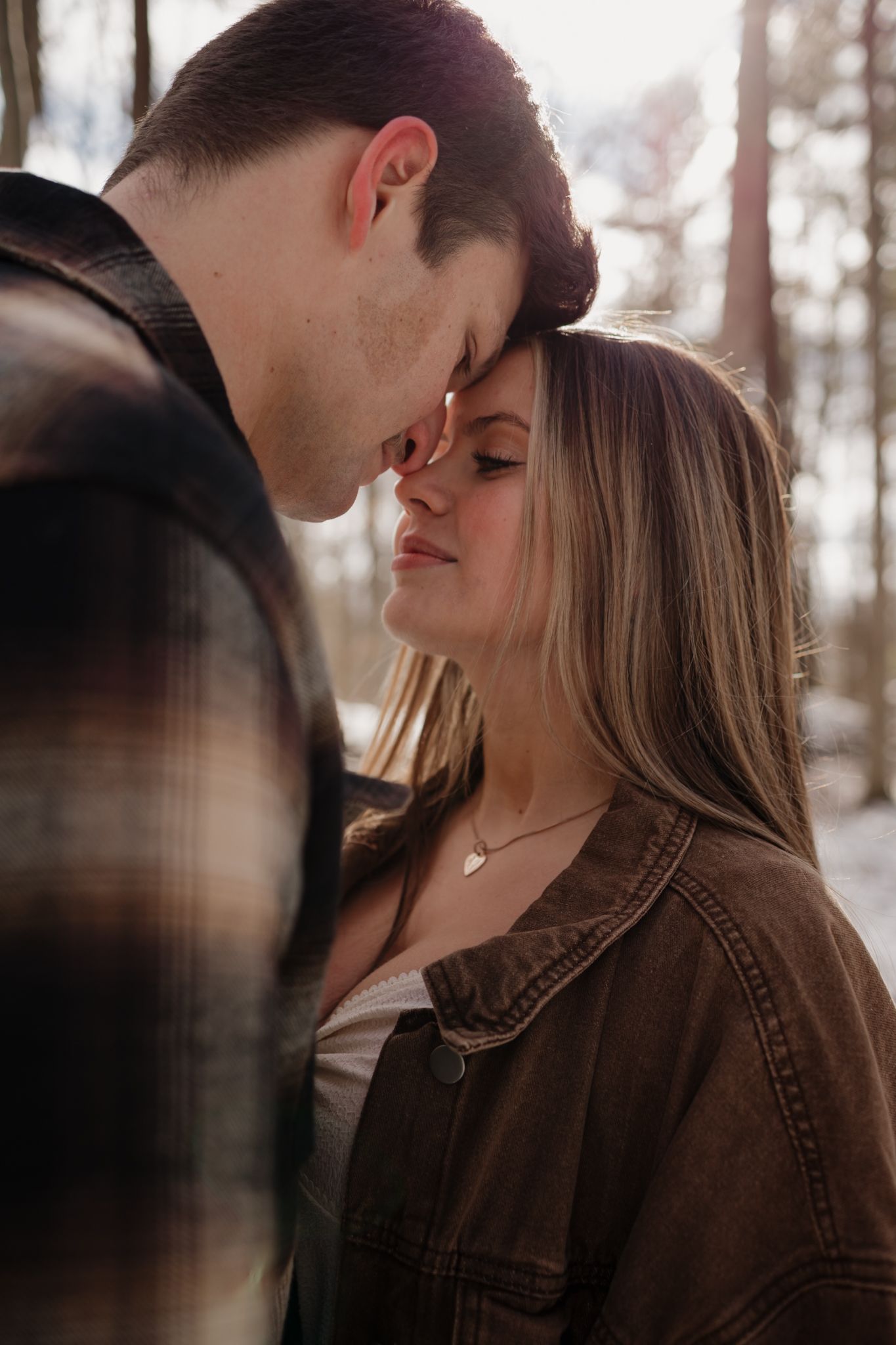 A romantic couple shares an intimate moment in brown leather jackets against a blurred autumn forest background.